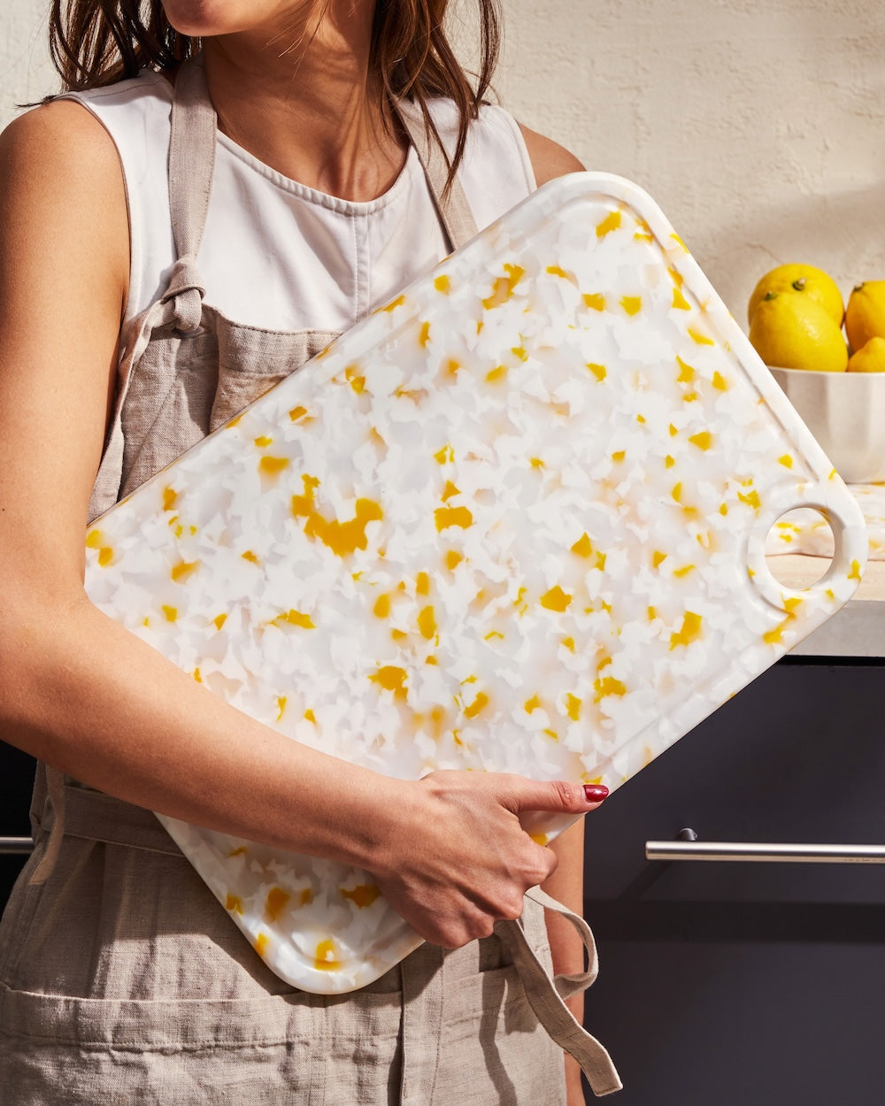Woman holding large recycled chopping board with yellow and white terrazzo pattern in kitchen