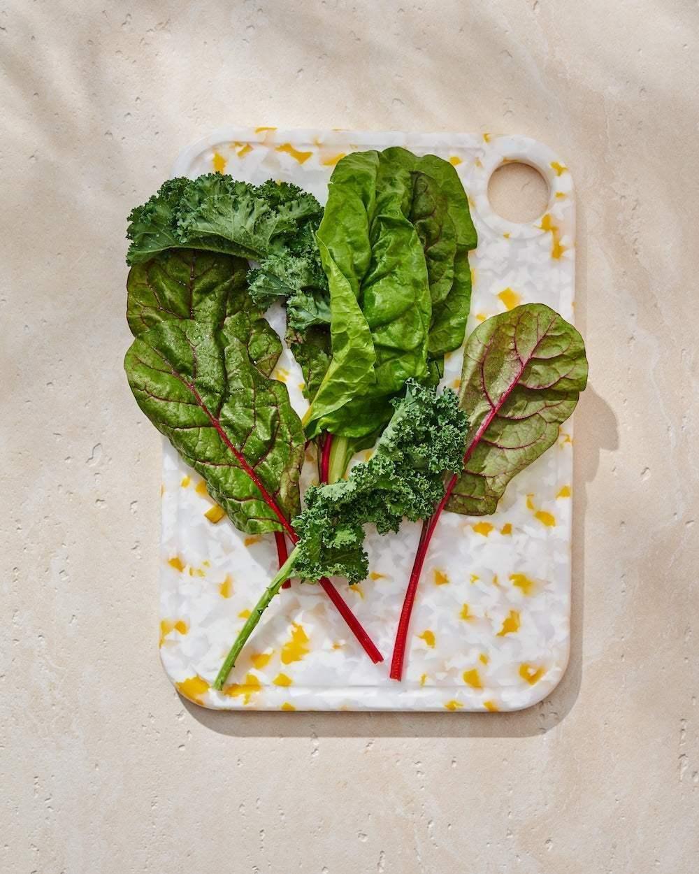 Colorful recycled chopping board with fresh kale and chard leaves on a neutral surface