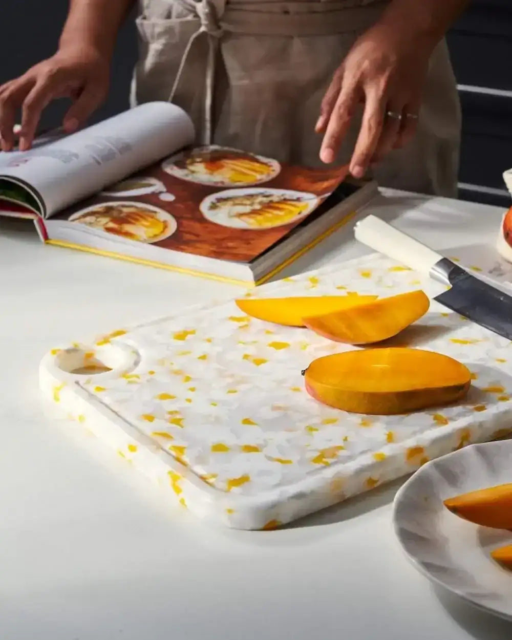 Juicy lemon meringue recycled chopping board with sliced mango and chef reading cookbook