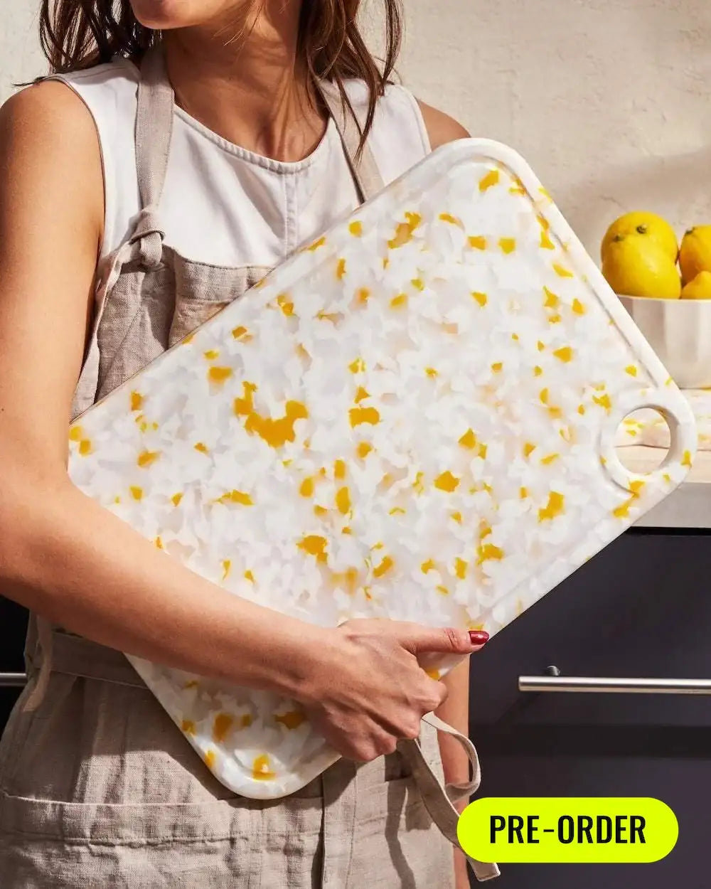 Woman holding a large recycled chopping board with white and yellow marbled design in kitchen