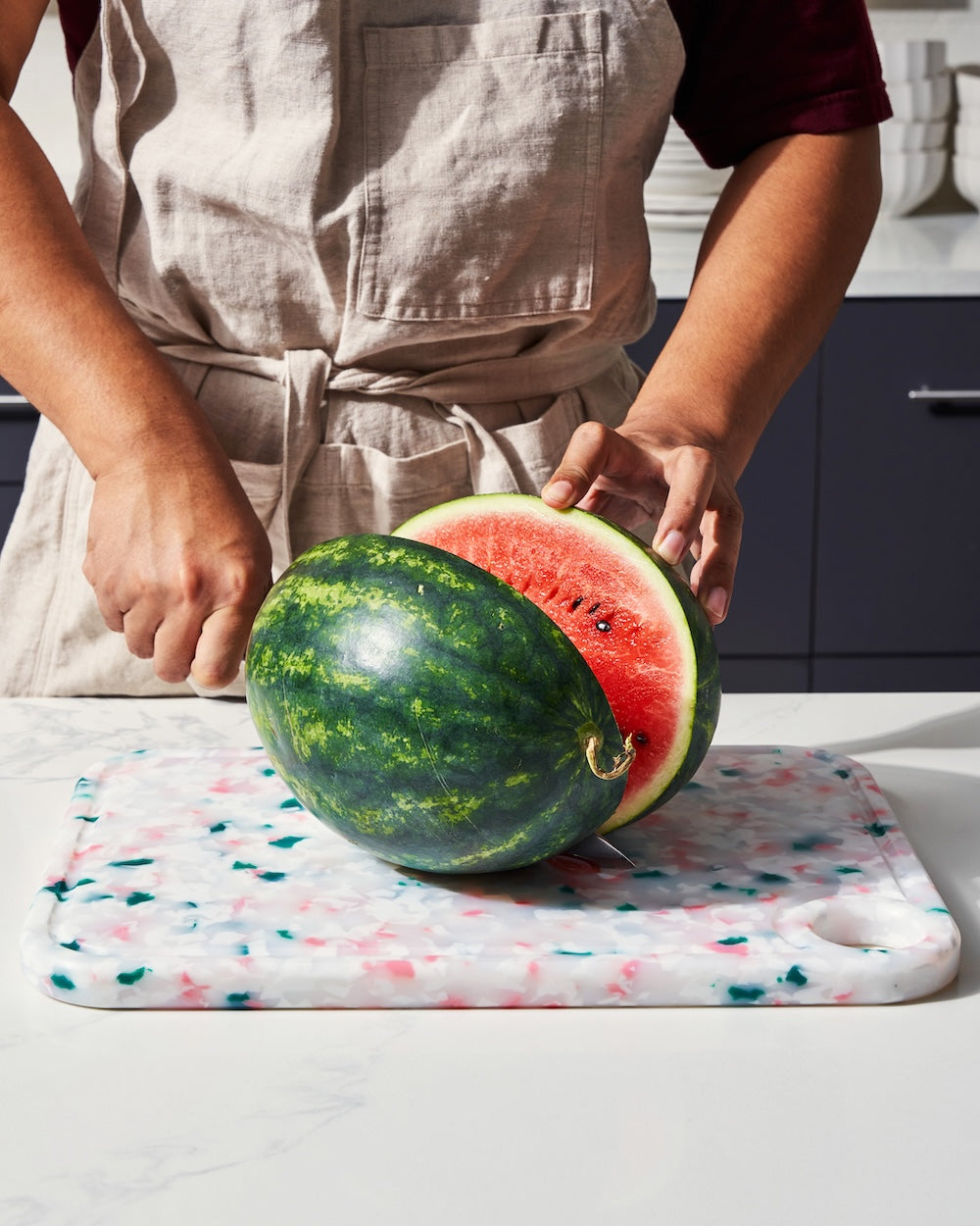 Person slicing fresh watermelon on a speckled recycled chopping board in a kitchen