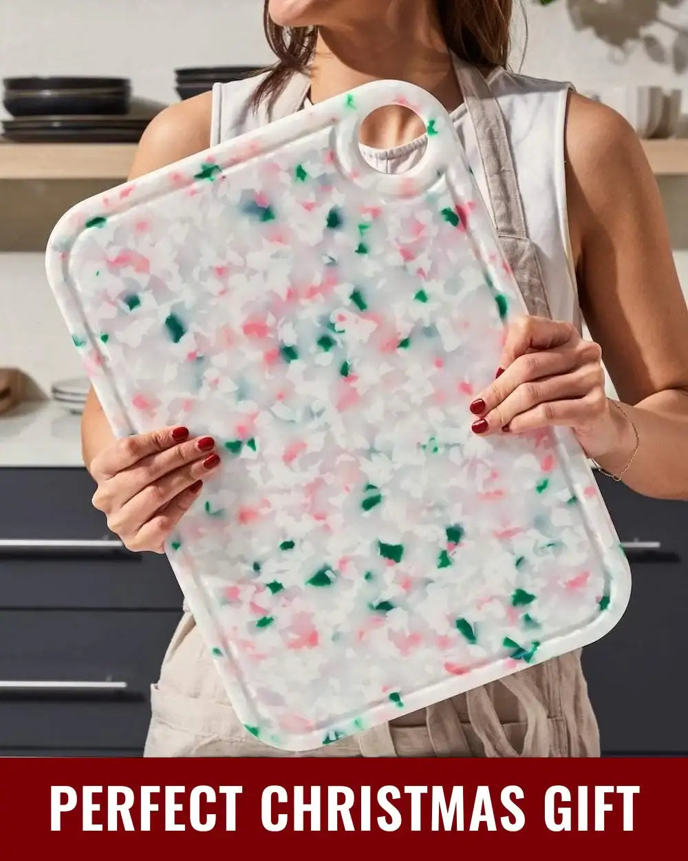 Person holding a festive speckled chopping board with red, green, and white colors in kitchen setting