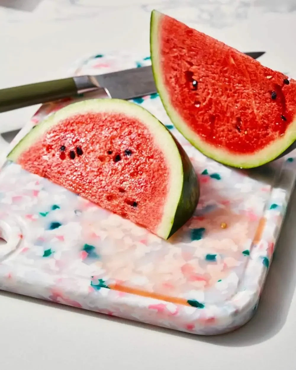 Sliced watermelon on a colorful recycled chopping board with a kitchen knife