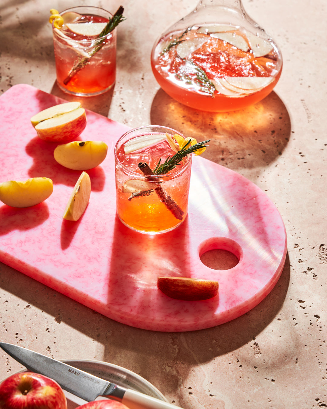 Pink recycled chopping board with apple slices, knife, and two glasses of fruit cocktails