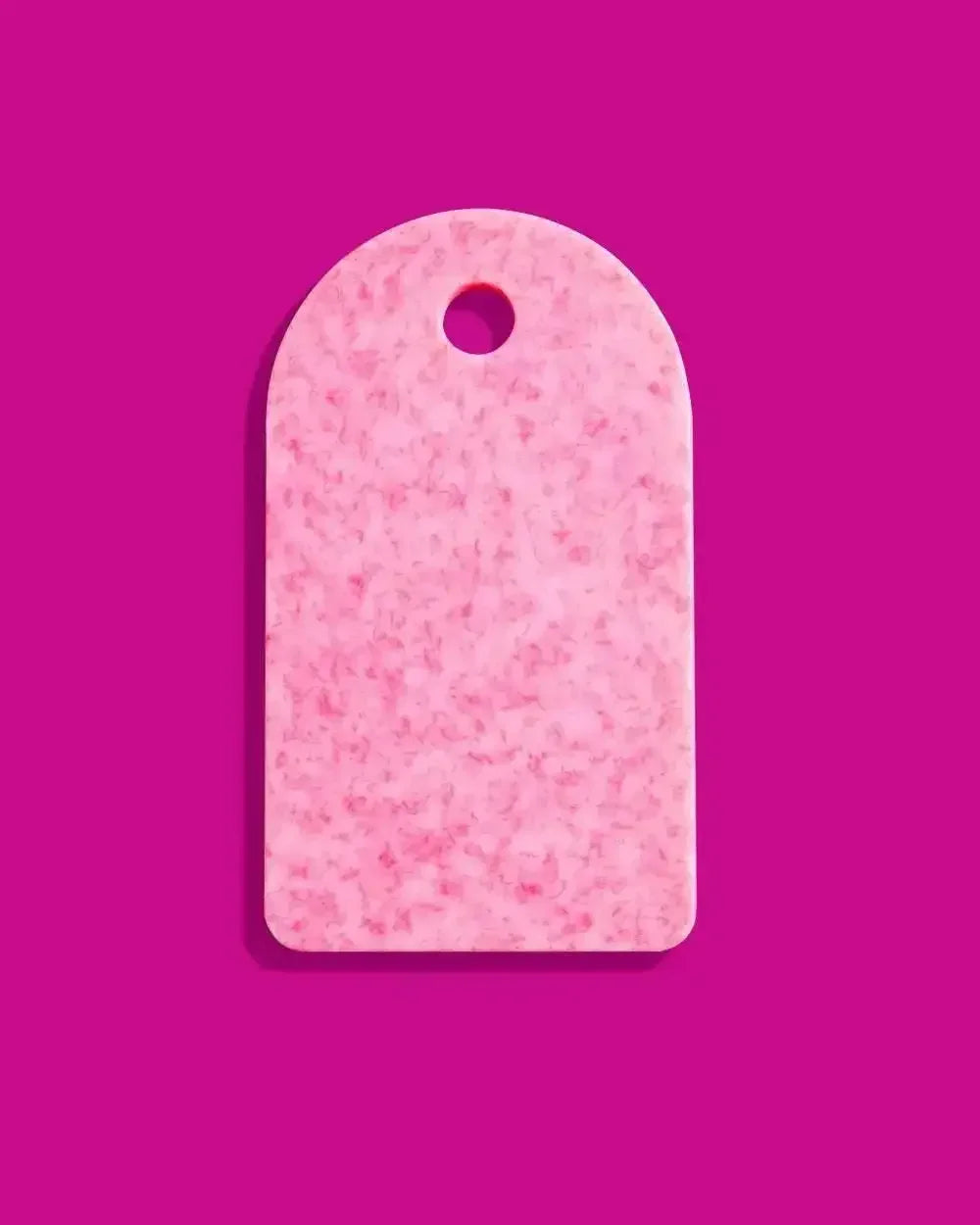 Rectangular pink recycled chopping board with rounded top and hanging hole on a purple background