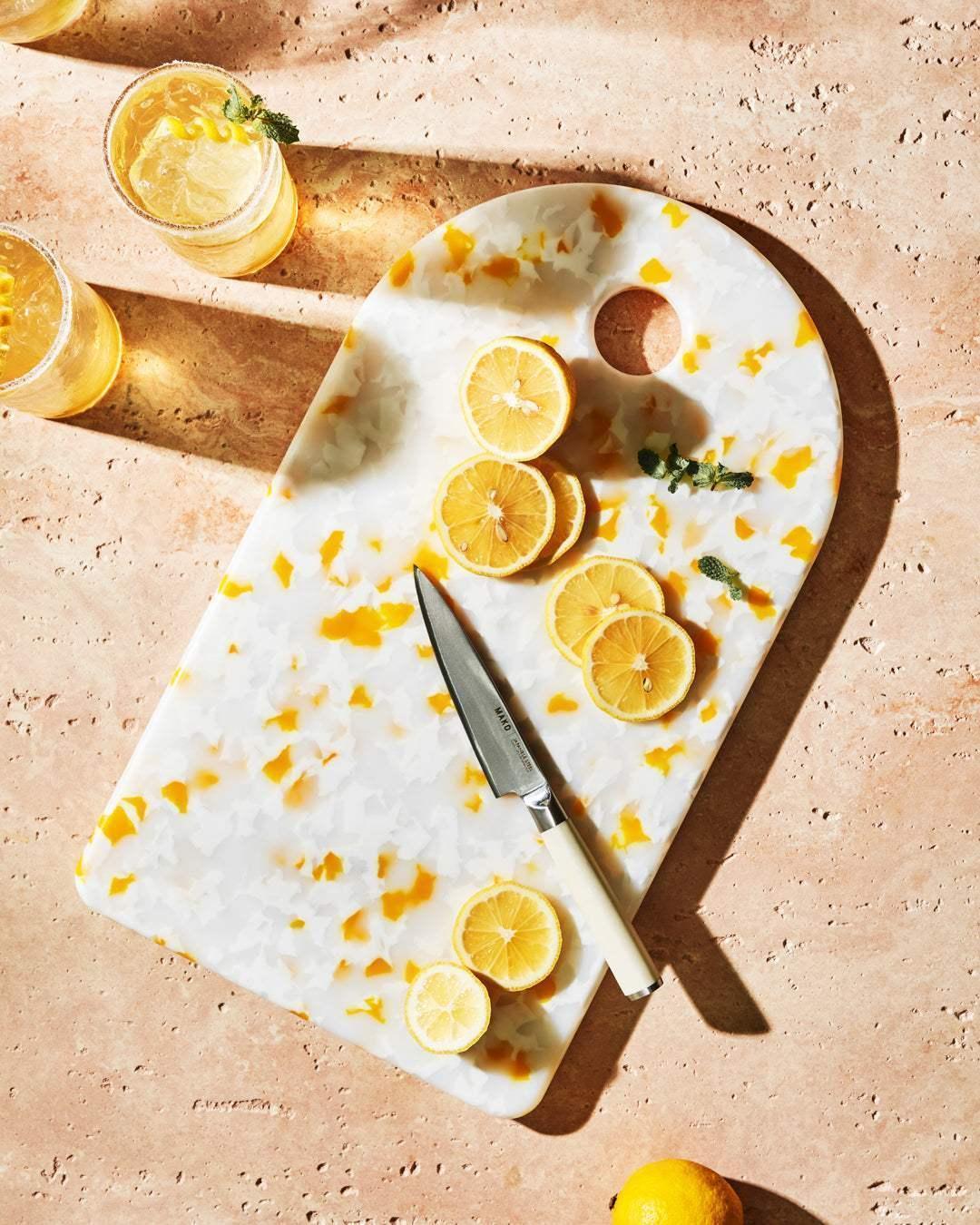 Asoke chopping board by Marion Grasby with sliced lemons and Mako knife on textured surface