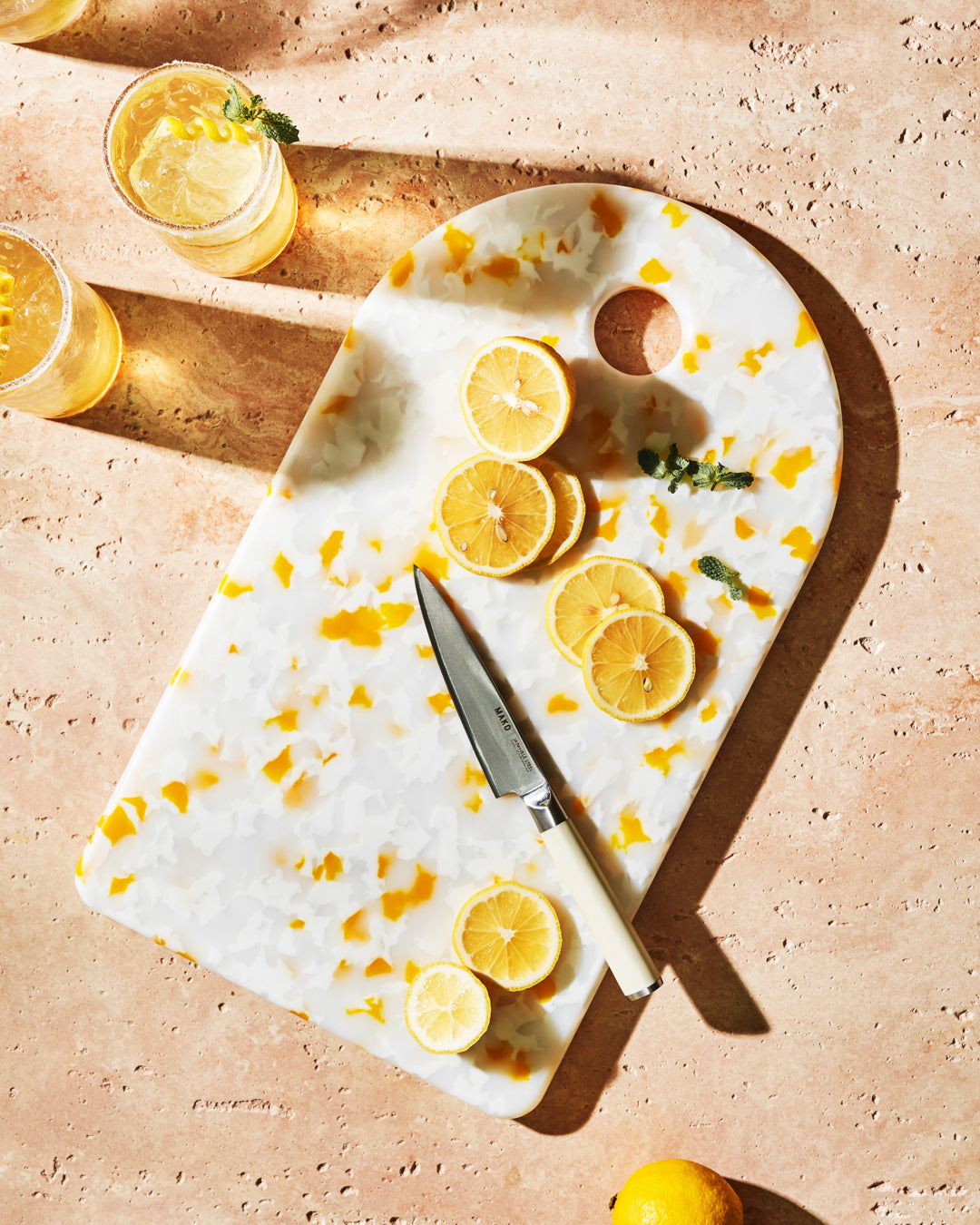 Recycled resin chopping board with yellow accents, sliced lemons, and knife on stone countertop