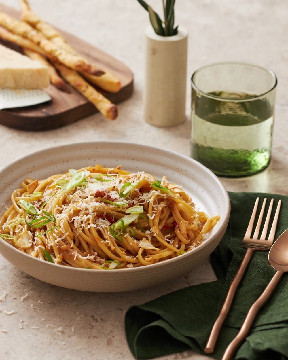 Ceramic dinner plate set with pasta, breadsticks, and gold cutlery on a neutral table setting