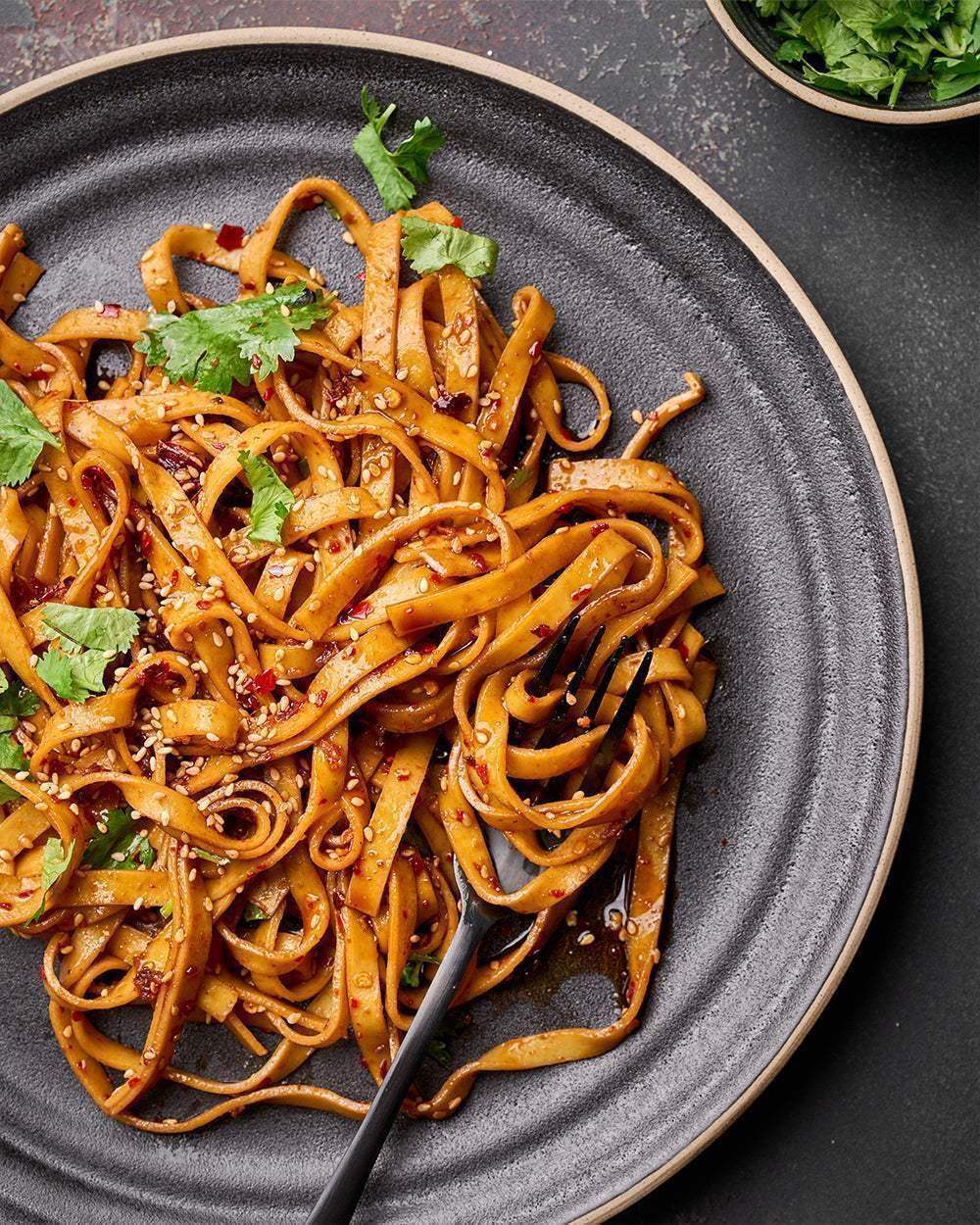 Anaya Charcoal 24-piece dinnerware set by Marion Grasby featuring dark textured plate with spicy noodles garnished with cilantro