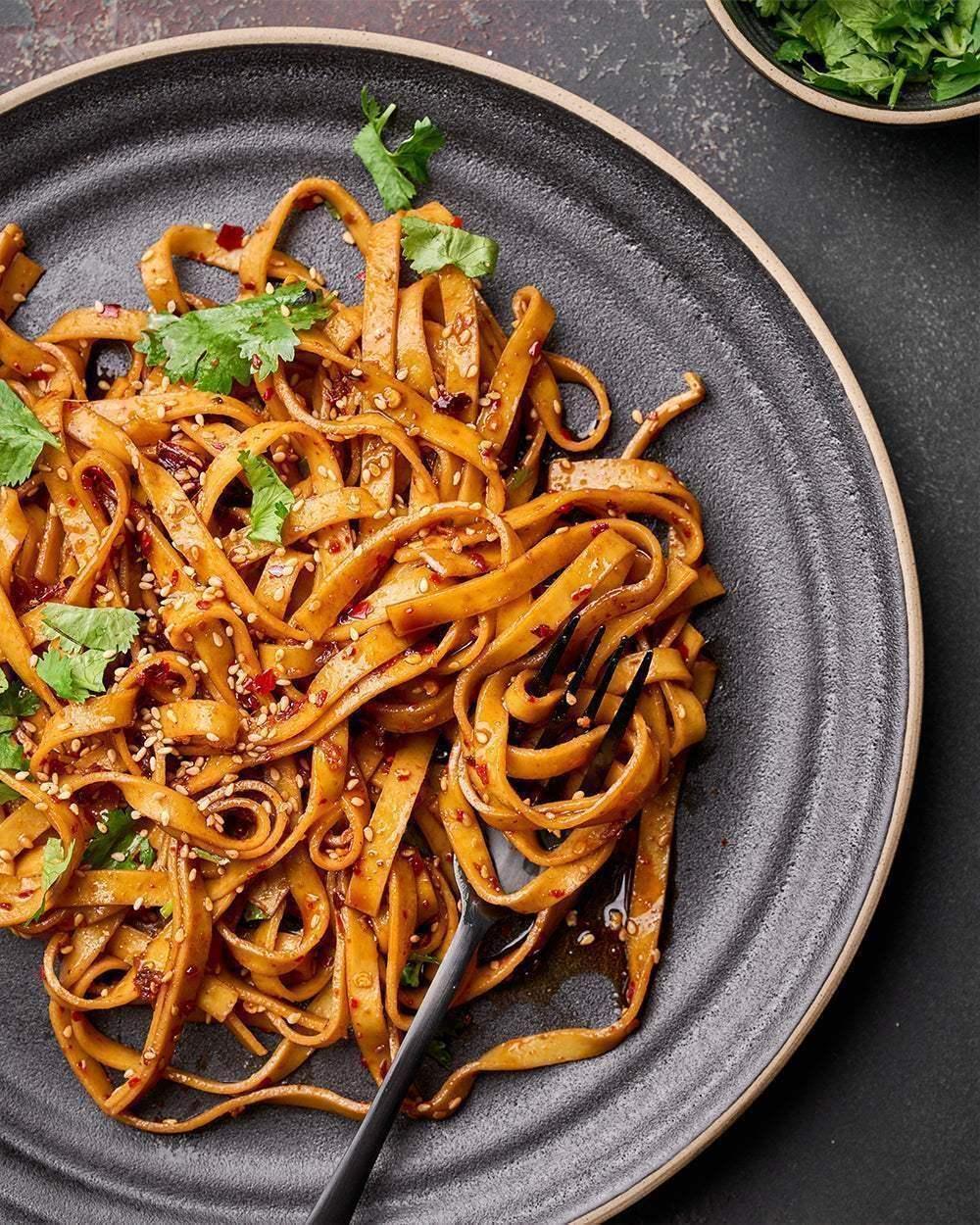 Charcoal stoneware dinner plate with noodles, fresh herbs and sesame seeds, black fork resting on plate