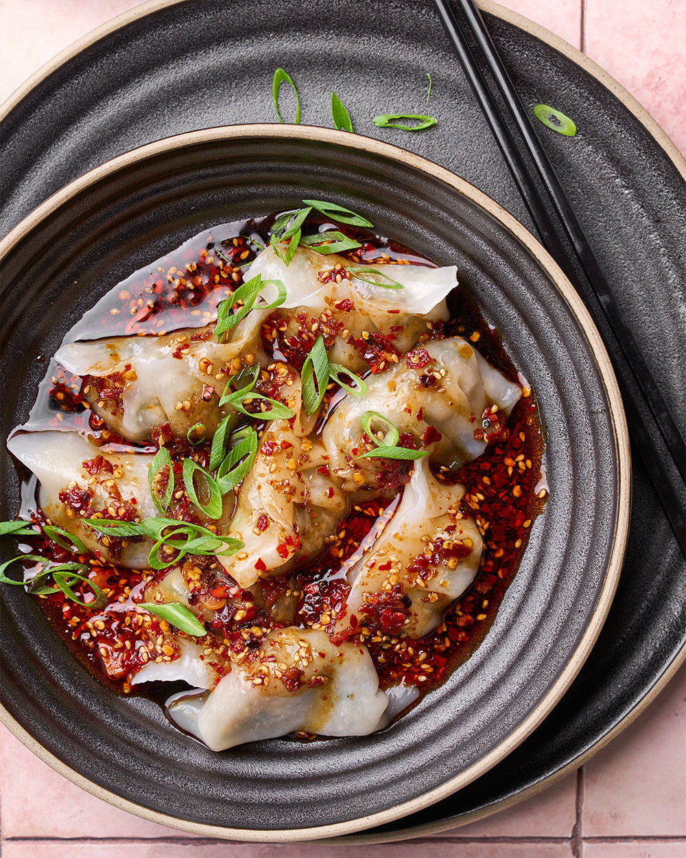 Charcoal textured dinnerware set with dumplings in chili oil, garnished with scallions