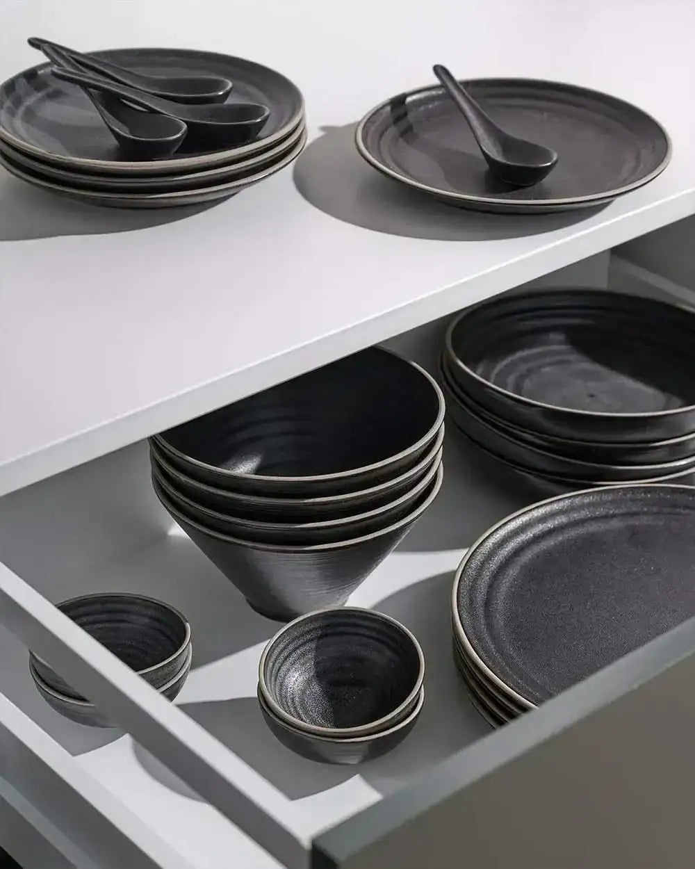 Asoke charcoal dinnerware set by Marion Grasby with plates, bowls, and spoons in a kitchen drawer
