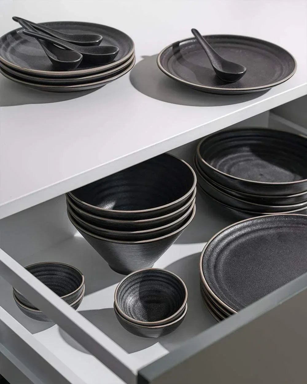 Asoke charcoal dinnerware set by Marion Grasby with plates, bowls, and spoons in a kitchen drawer