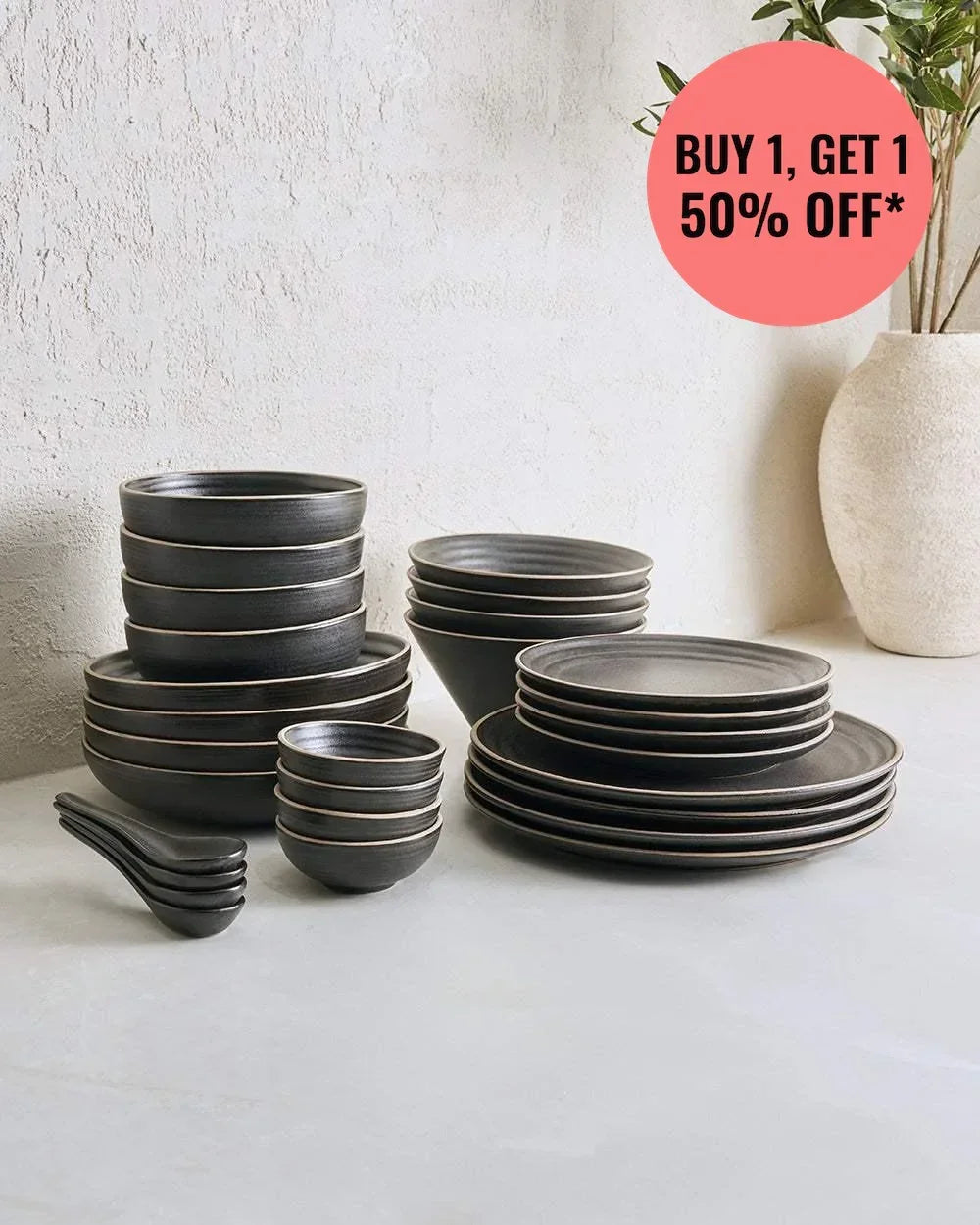 Marion Grasby Asoke charcoal 28-piece stoneware dinnerware set with bowls, plates, and spoons on white surface