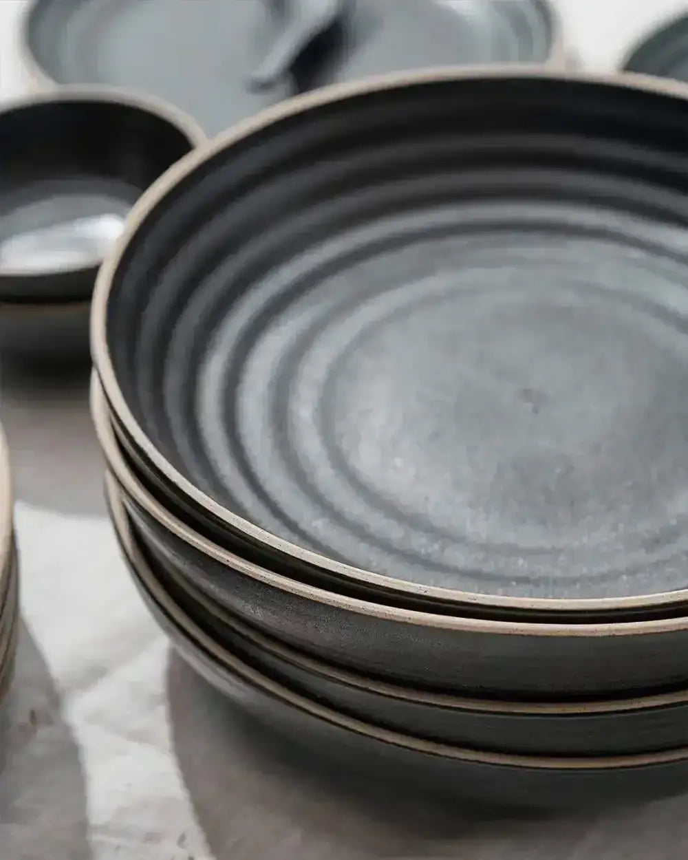 Stack of charcoal grey Asoke dinnerware plates and bowls with a textured, matte finish by Marion Grasby