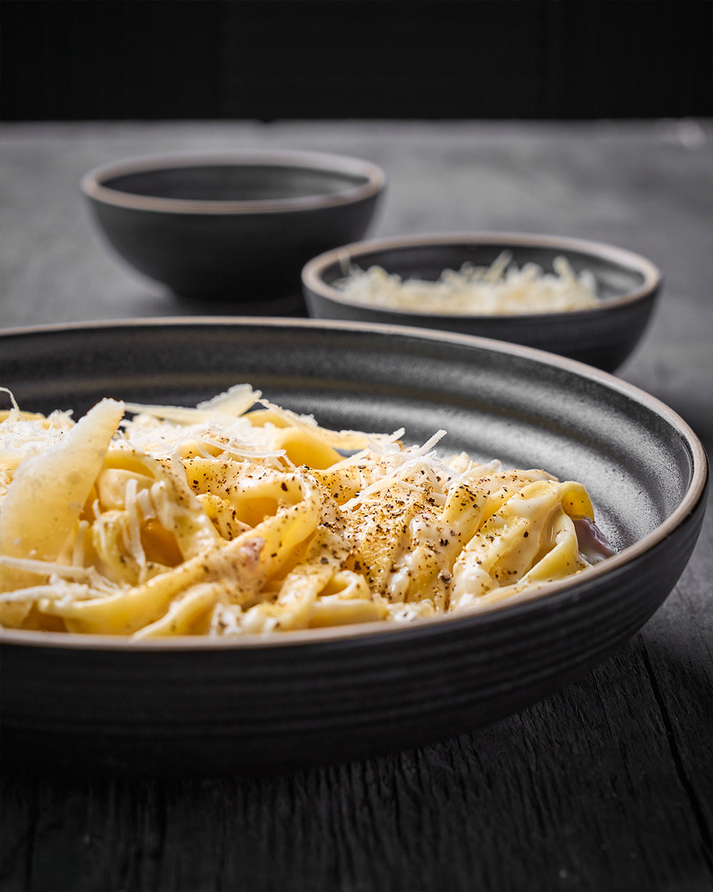 Charcoal ceramic pasta bowl set with fettuccine and grated cheese on rustic table