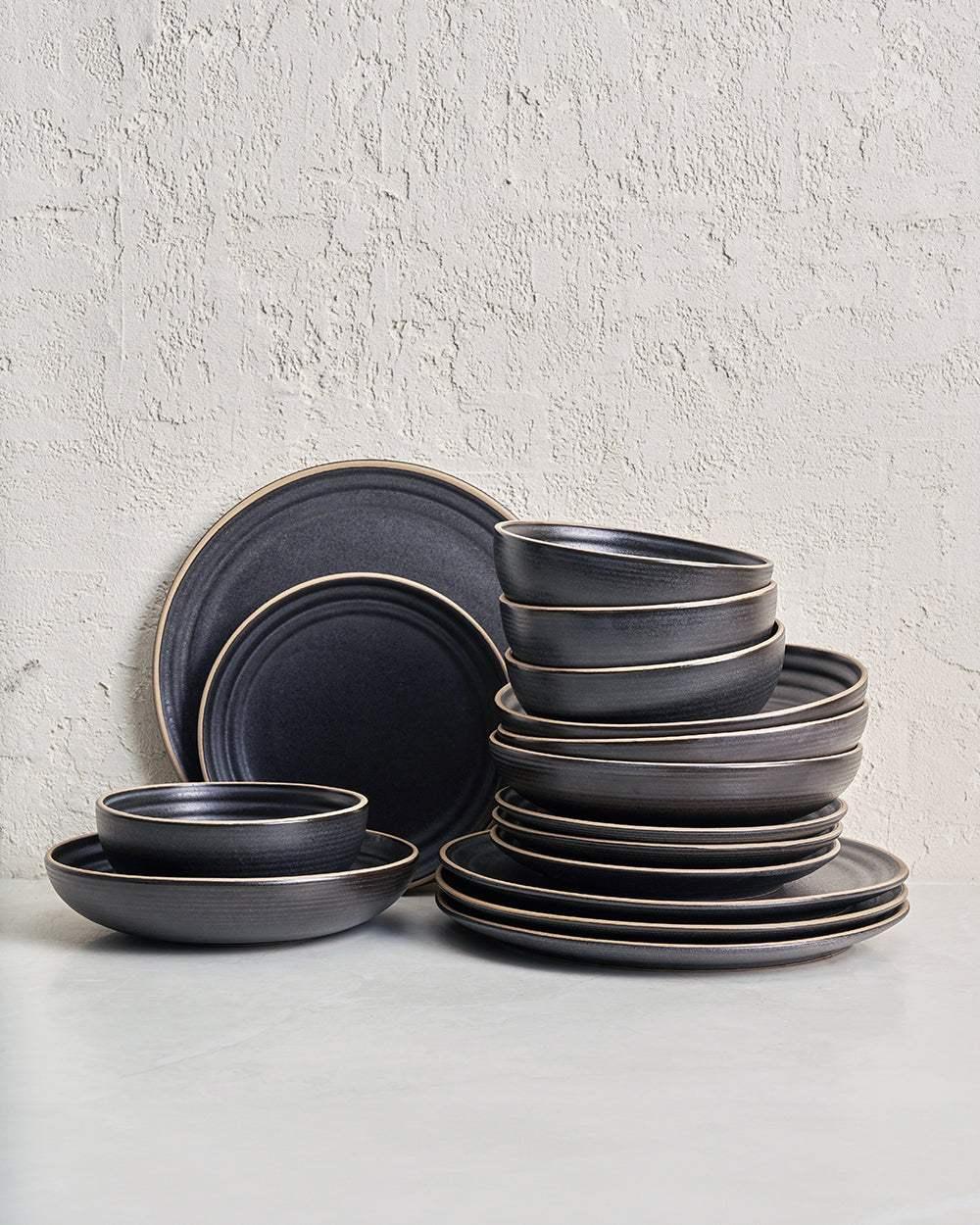 Matte charcoal ceramic dinnerware set with plates and bowls on a grey surface
