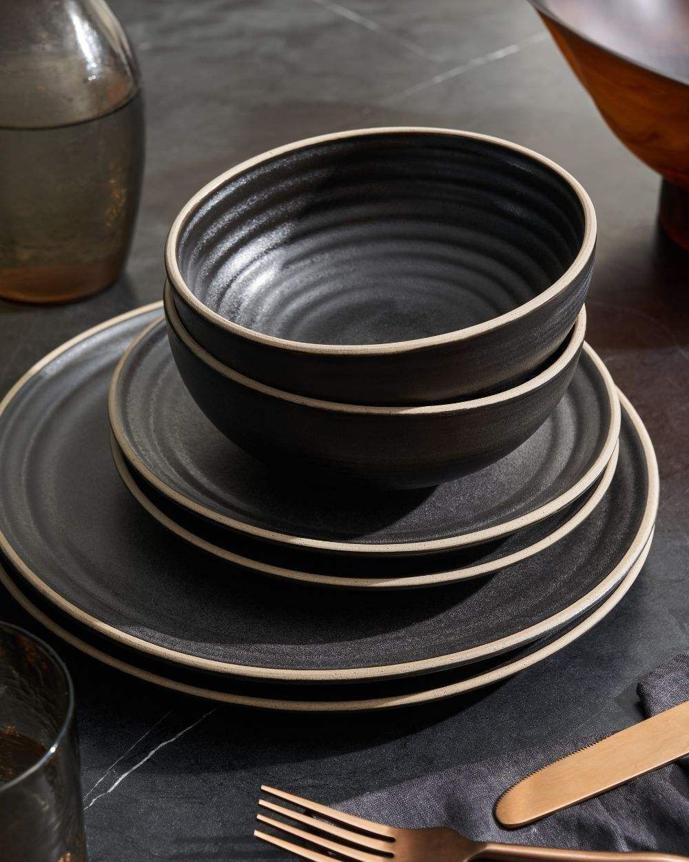 Asoke charcoal starter dinnerware set by Marion Grasby with stacked bowls and plates on dark table