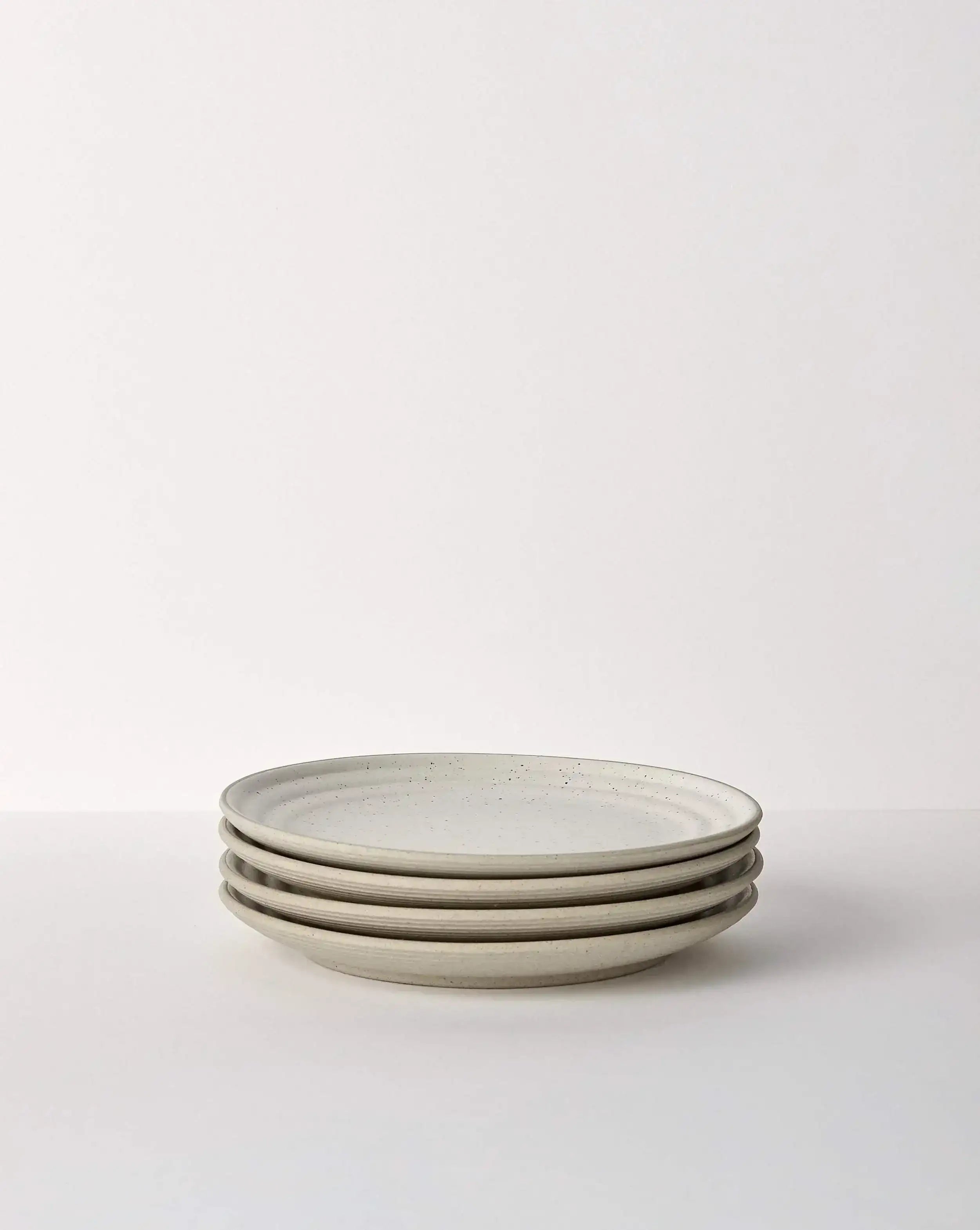Stack of four beige speckled ceramic dinner plates on a white surface, minimal design