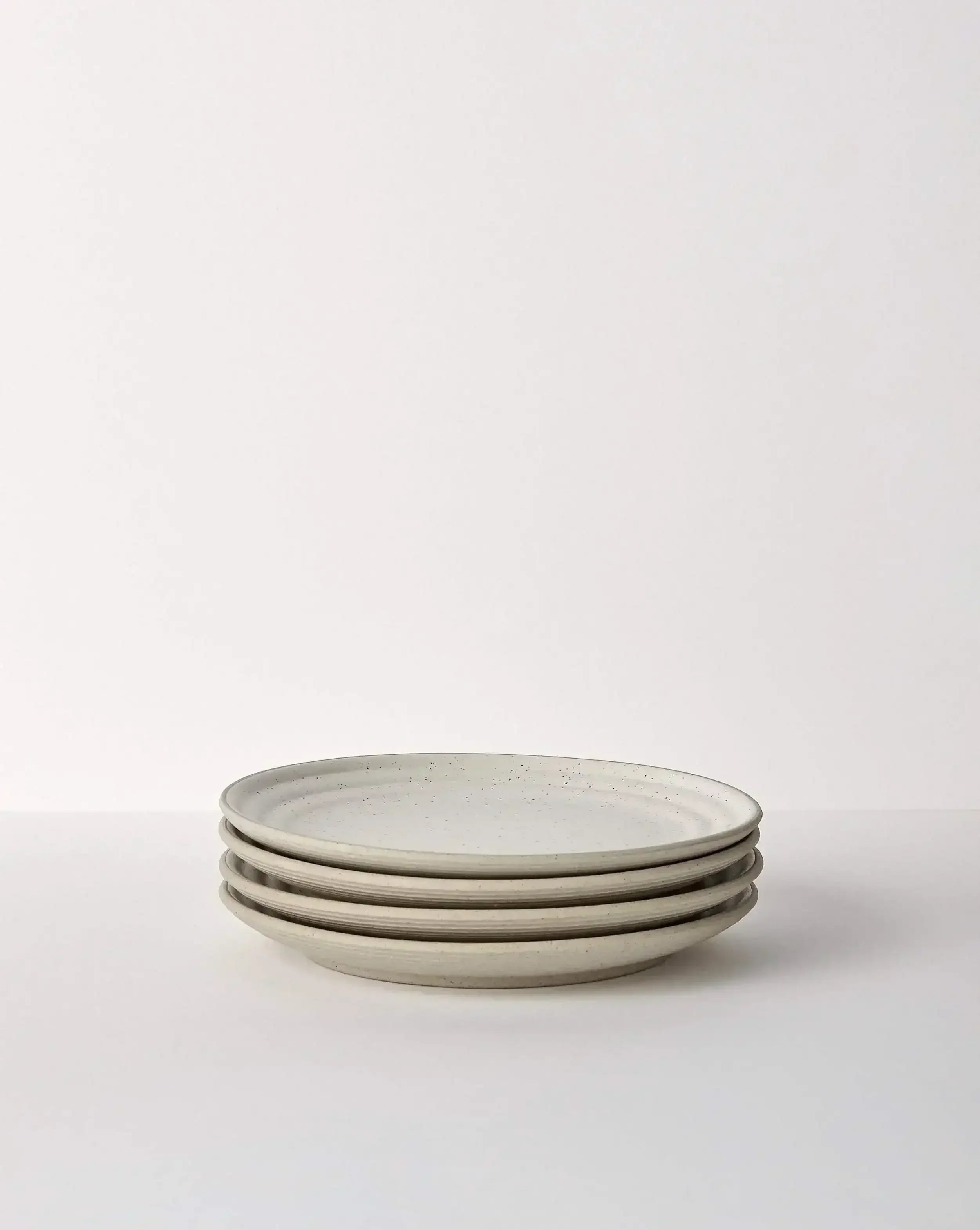 Stack of four speckled ceramic dinner plates in neutral tones on a white background