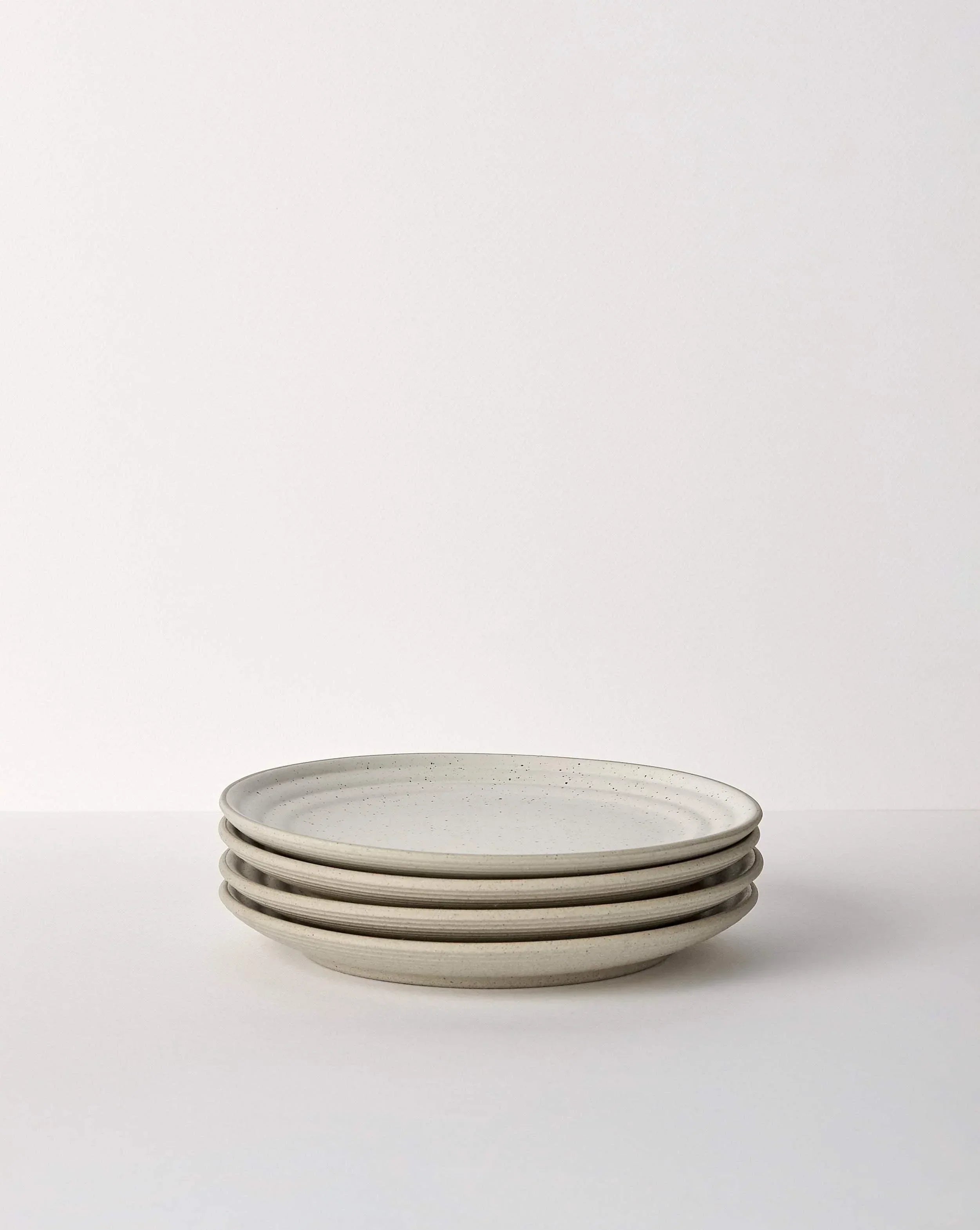 Stack of four beige speckled ceramic dinner plates on a white surface, minimal design