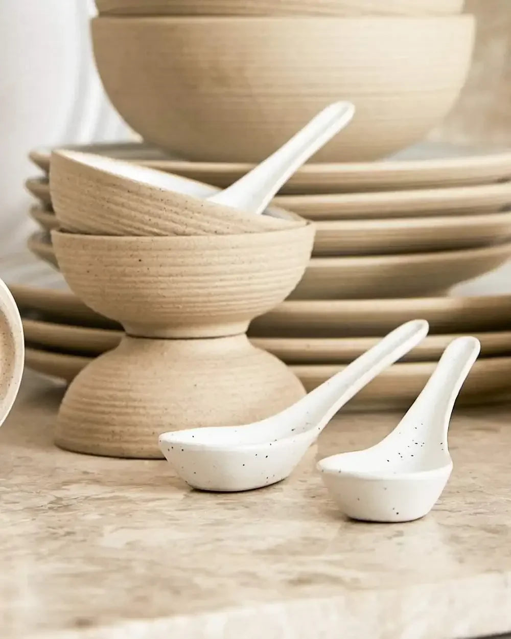 Neutral-toned stacked mini bowls with two white ceramic spoons on a marble surface