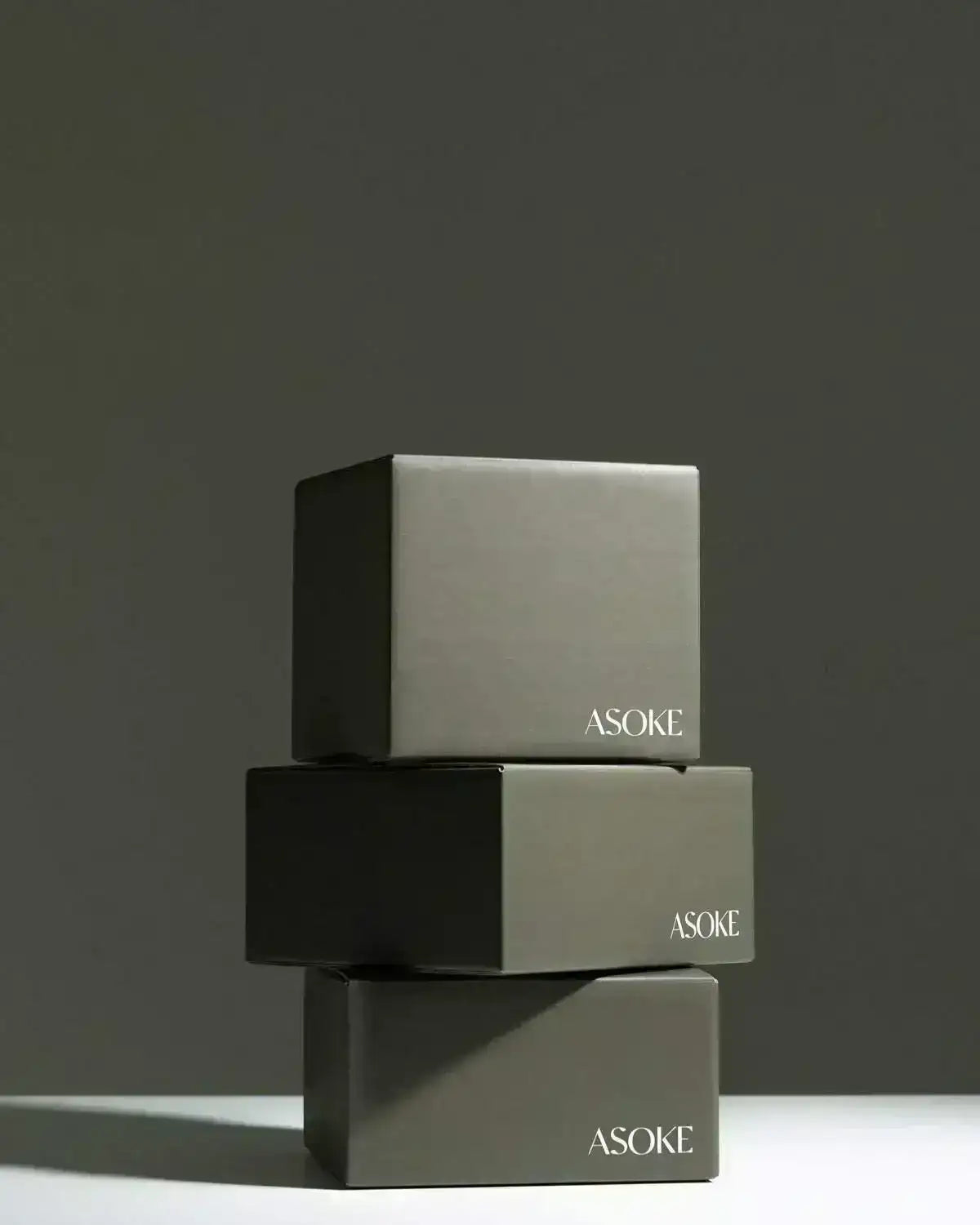 Three stacked minimalist dark green Asoke noodle gift boxes by Marion Grasby against gray backdrop