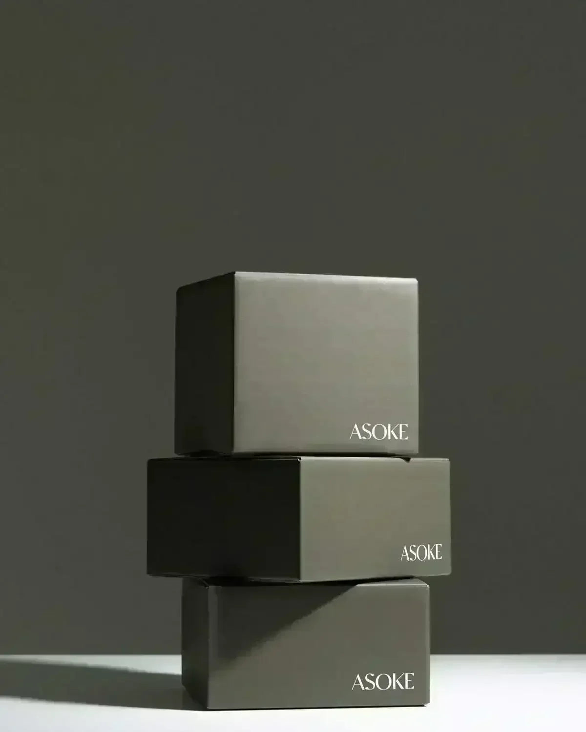Stack of three matte gray ASOKE gift boxes with minimalist design on neutral background