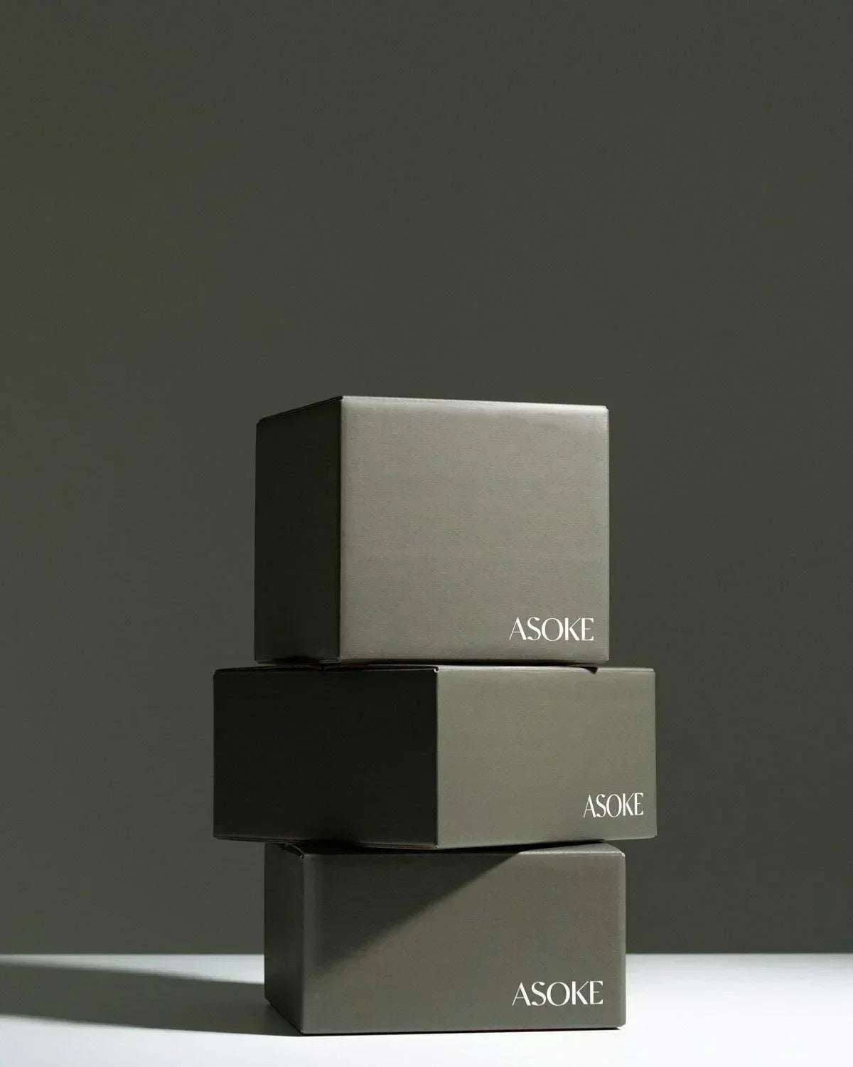 Three stacked minimalist dark green Asoke noodle gift boxes by Marion Grasby against gray backdrop