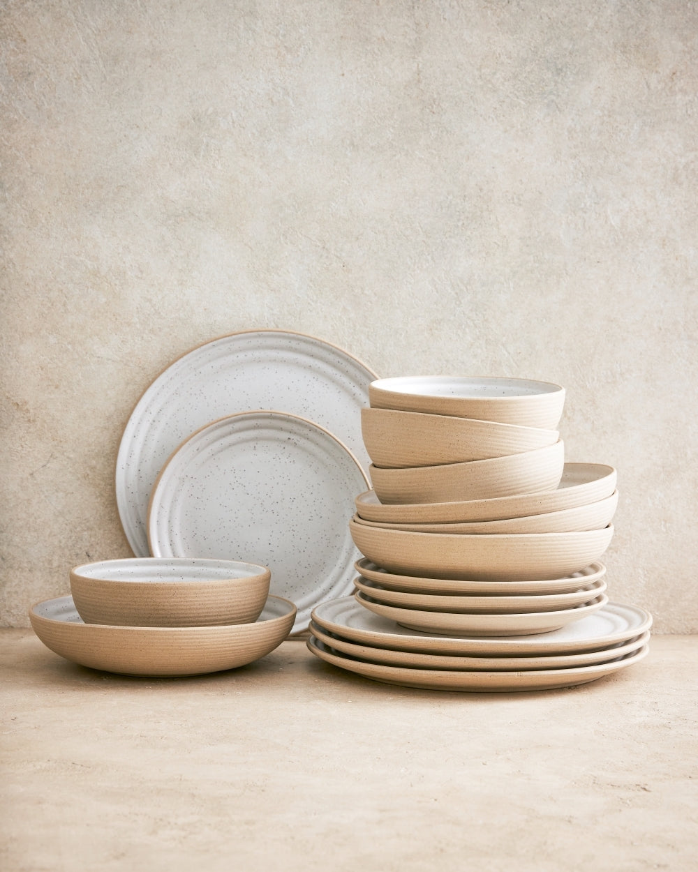 Set of beige and white stoneware bowls and plates stacked on a neutral surface.