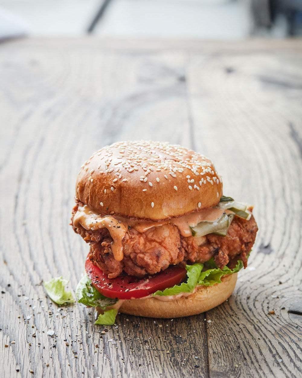 Crispy fried chicken sandwich with lettuce, tomato, pickles, and sauce on sesame bun