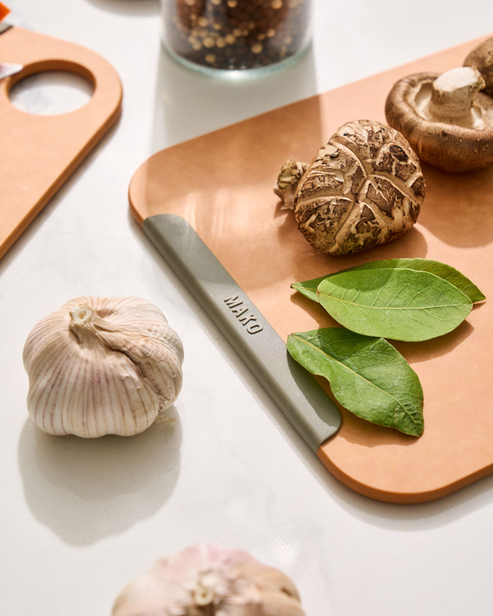Non-slip MAKO chopping board with garlic, mushrooms, and fresh green leaves on kitchen counter