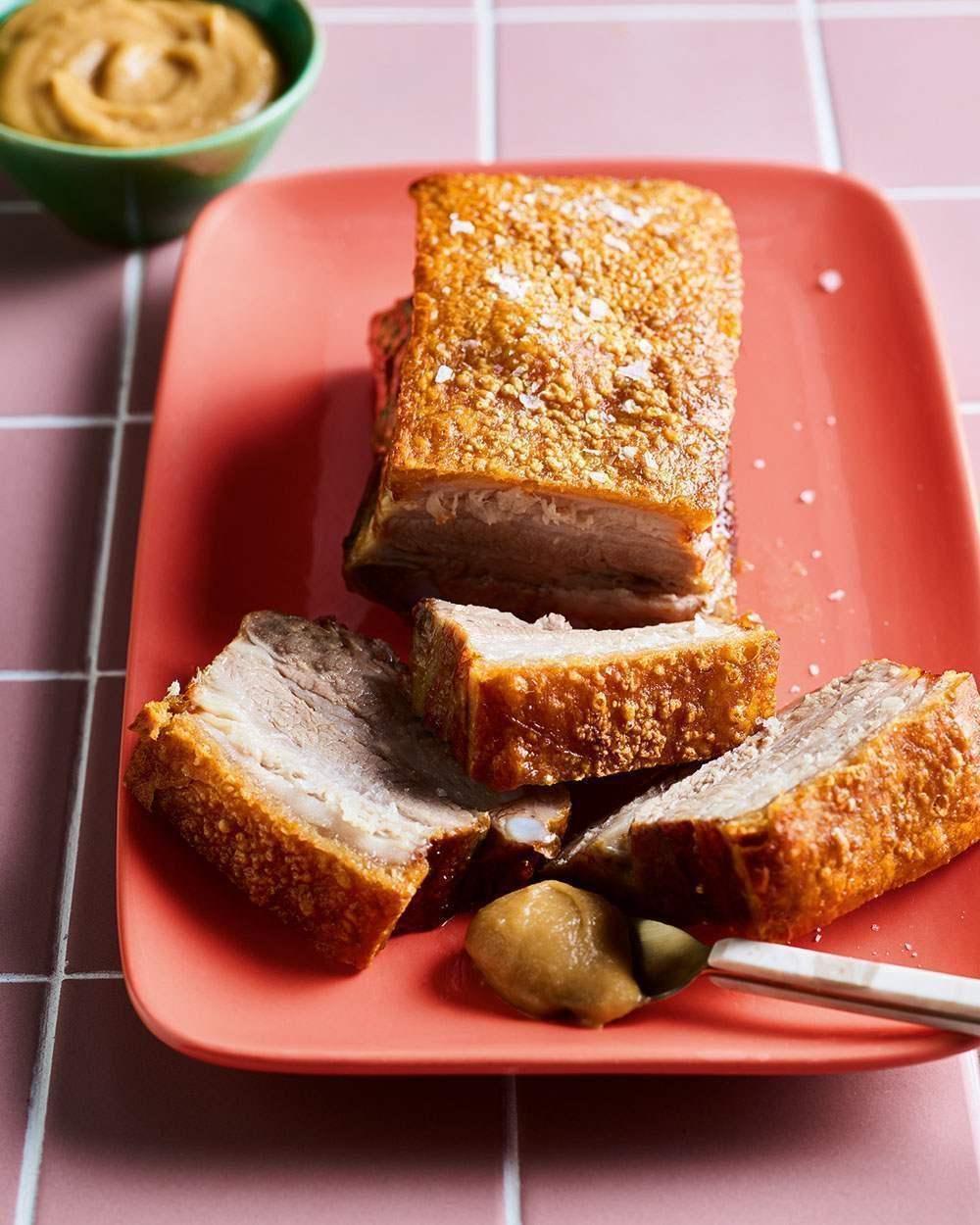 Crispy roast pork belly slices on a coral plate with mustard and dipping sauce