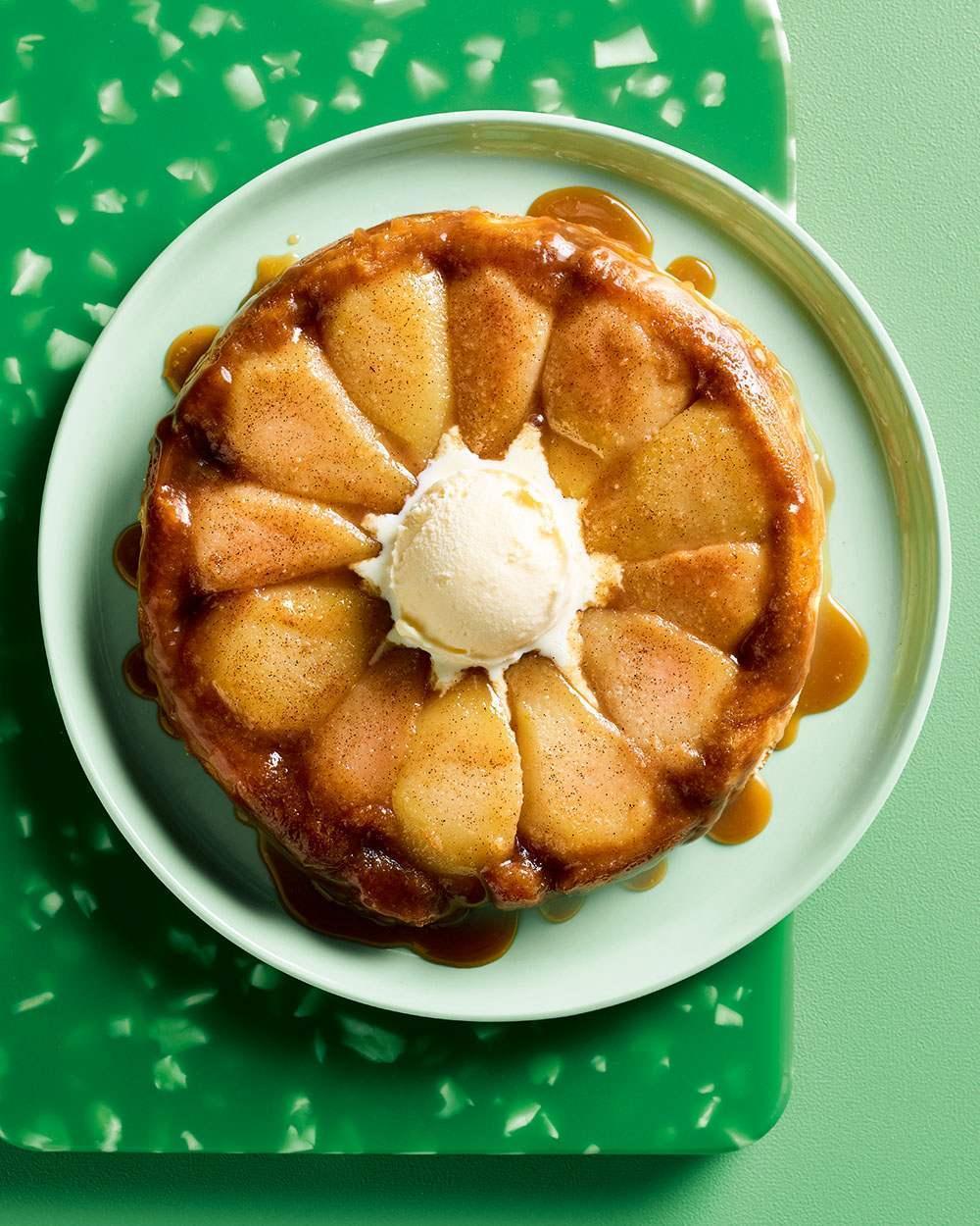 Pear tarte tatin dessert topped with vanilla ice cream on a white plate over a green tray