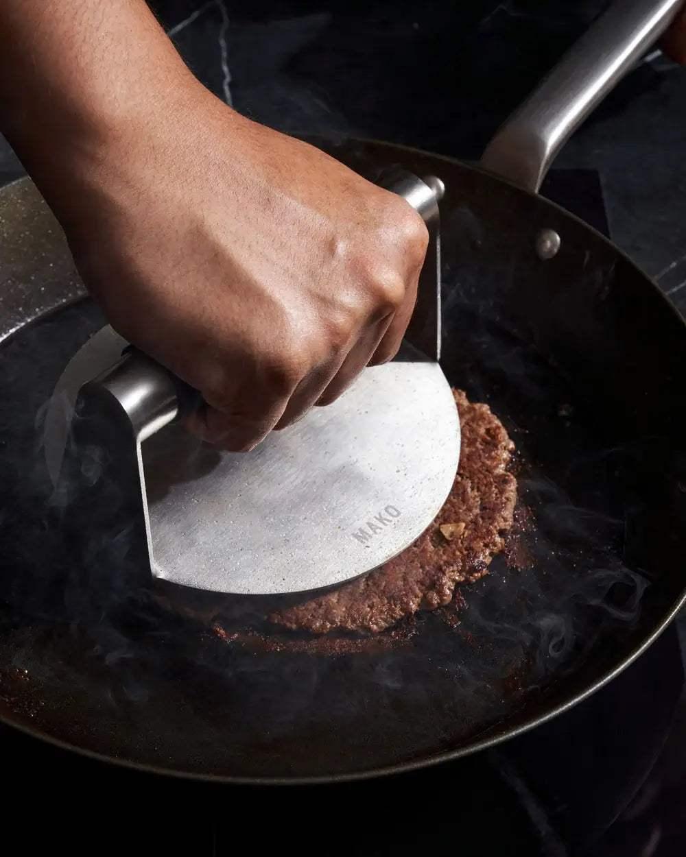 MAKO Black Steel Steak Pan - CookDineHost included press being used on burger patty