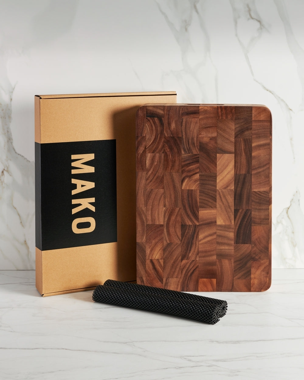 End grain wooden chopping board with non-slip mat and product box on marble countertop