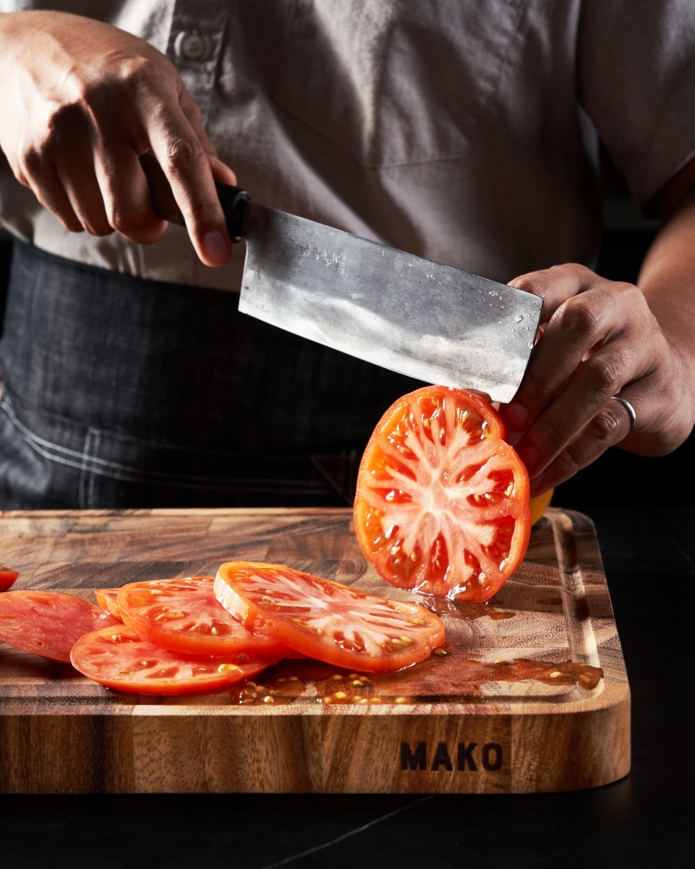 Slicing ripe tomato on wooden chopping board with chef knife