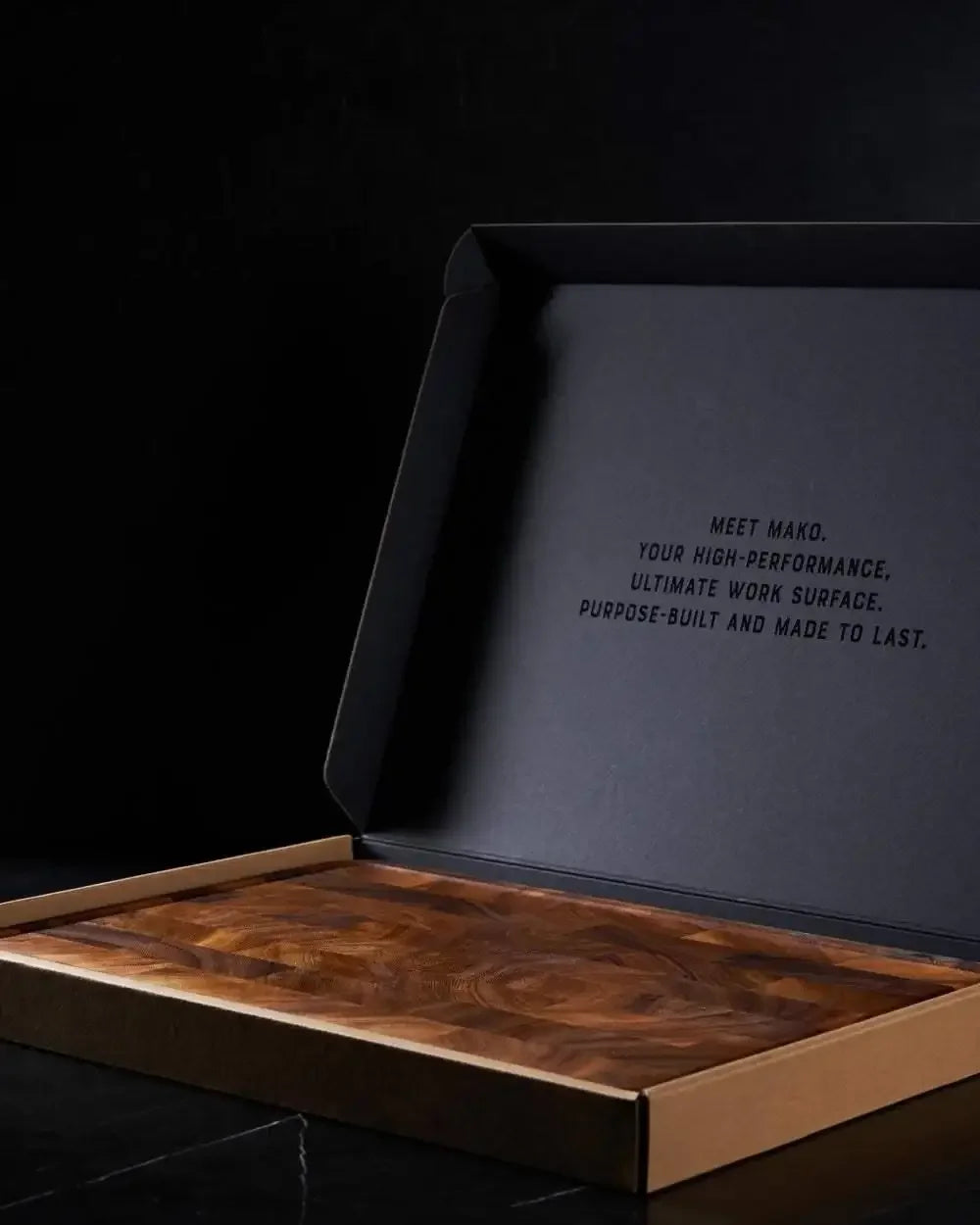 End grain wooden chopping board in an open black box on a dark surface