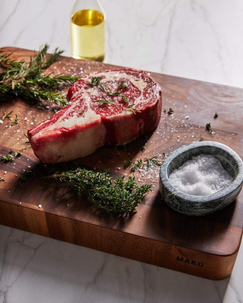 Marion Grasby Mako wooden butcher block with seasoned ribeye steak, rosemary, coarse salt in marble bowl