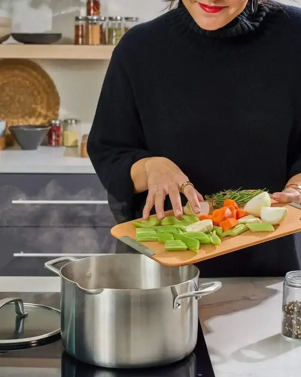 Person adding chopped vegetables from non-slip Mako wood fibre chopping board into steaming pot in modern kitchen