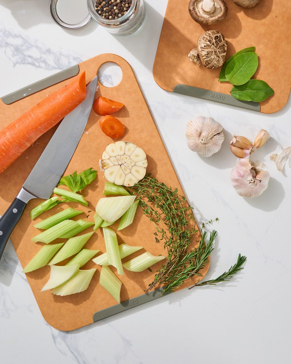 Non-slip wood fibre chopping board with knife, cut vegetables, herbs, and garlic on marble surface