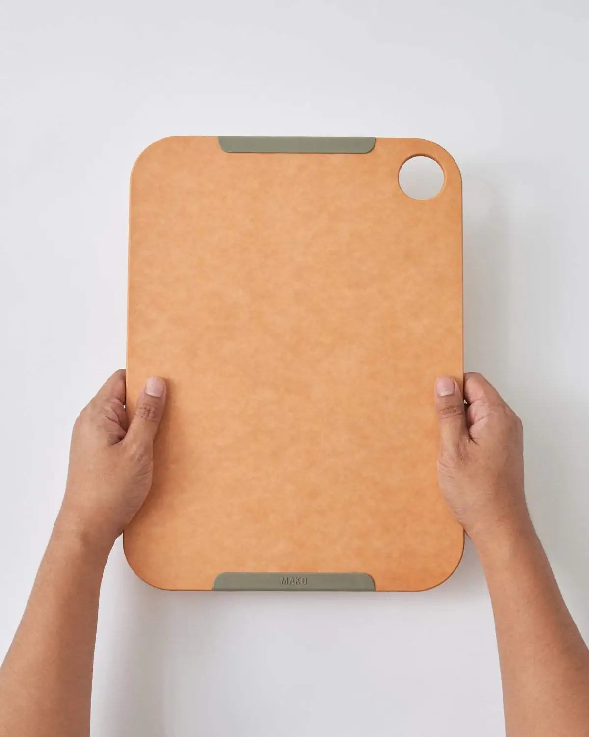 Hands holding a large Mako non-slip wood fibre chopping board with corner hole