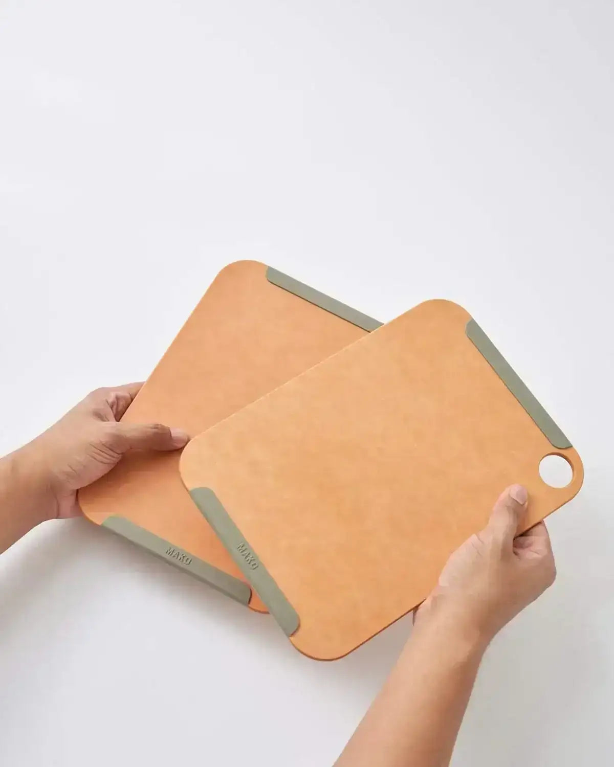 Hands holding two MAKO non-slip wood fibre chopping boards, small set, from CookDineHost.
