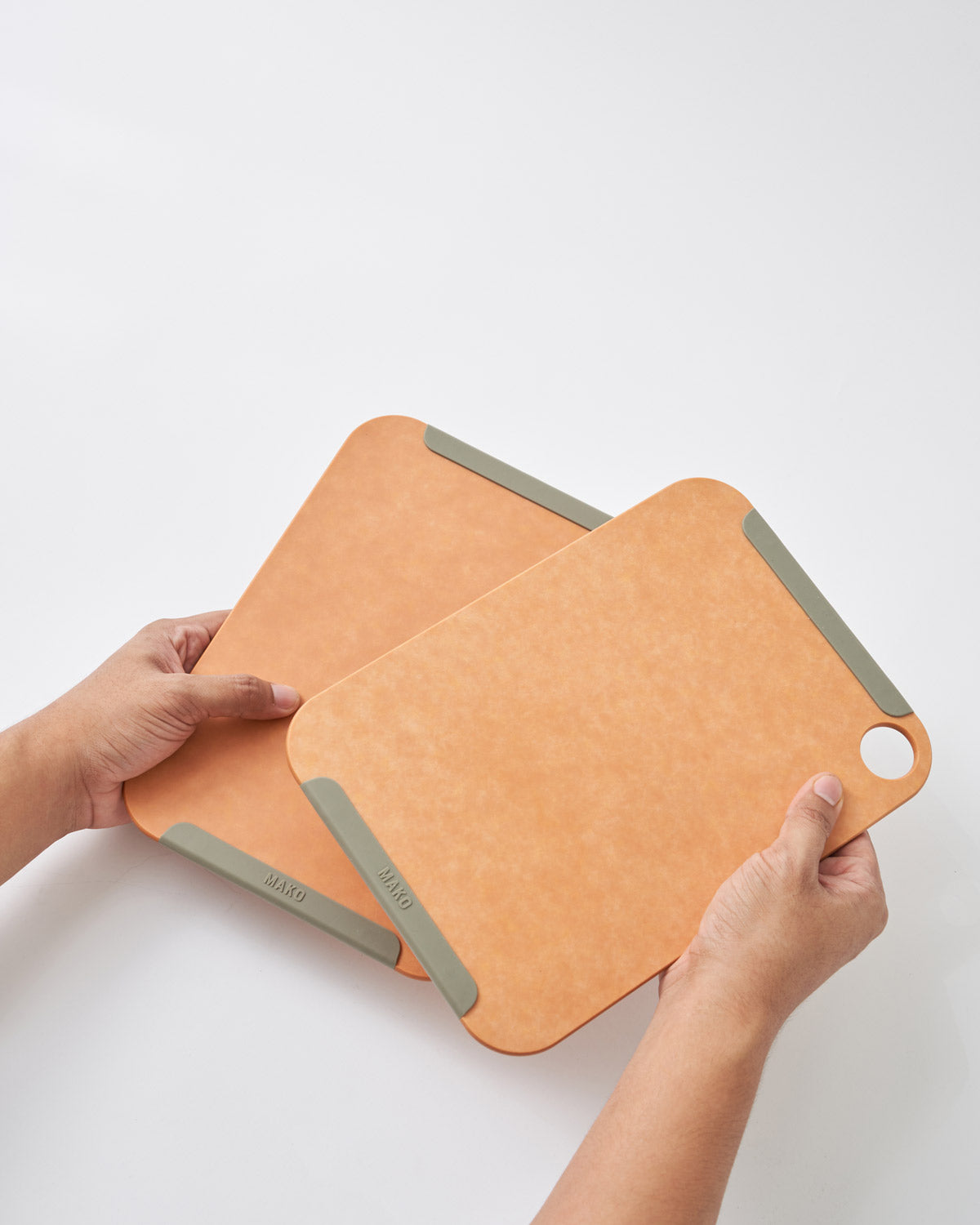 Hands holding two small non-slip wood fibre chopping boards with grey edges