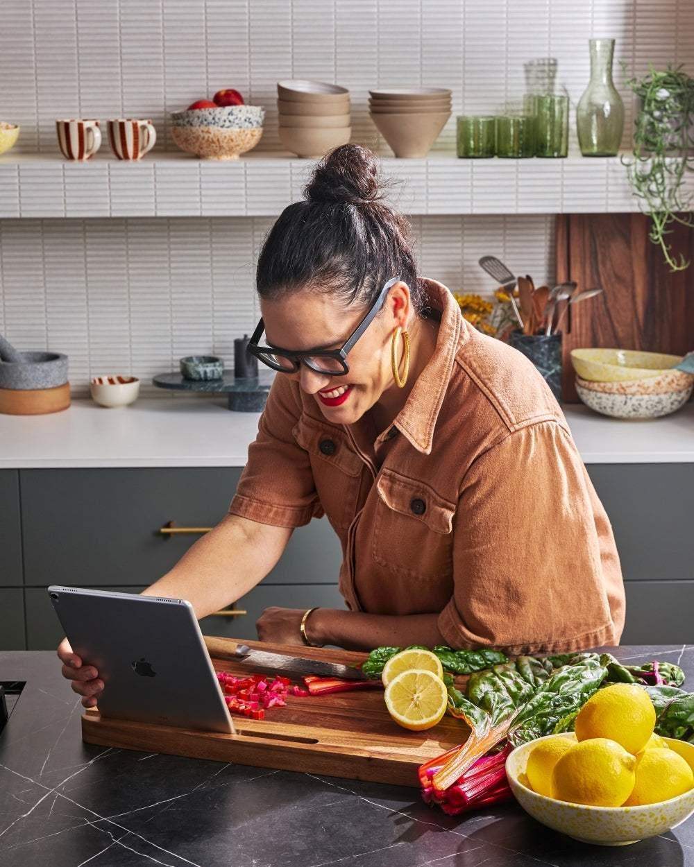 Woman using tablet on a Mako multi-use chopping board with lemons and greens in modern kitchen