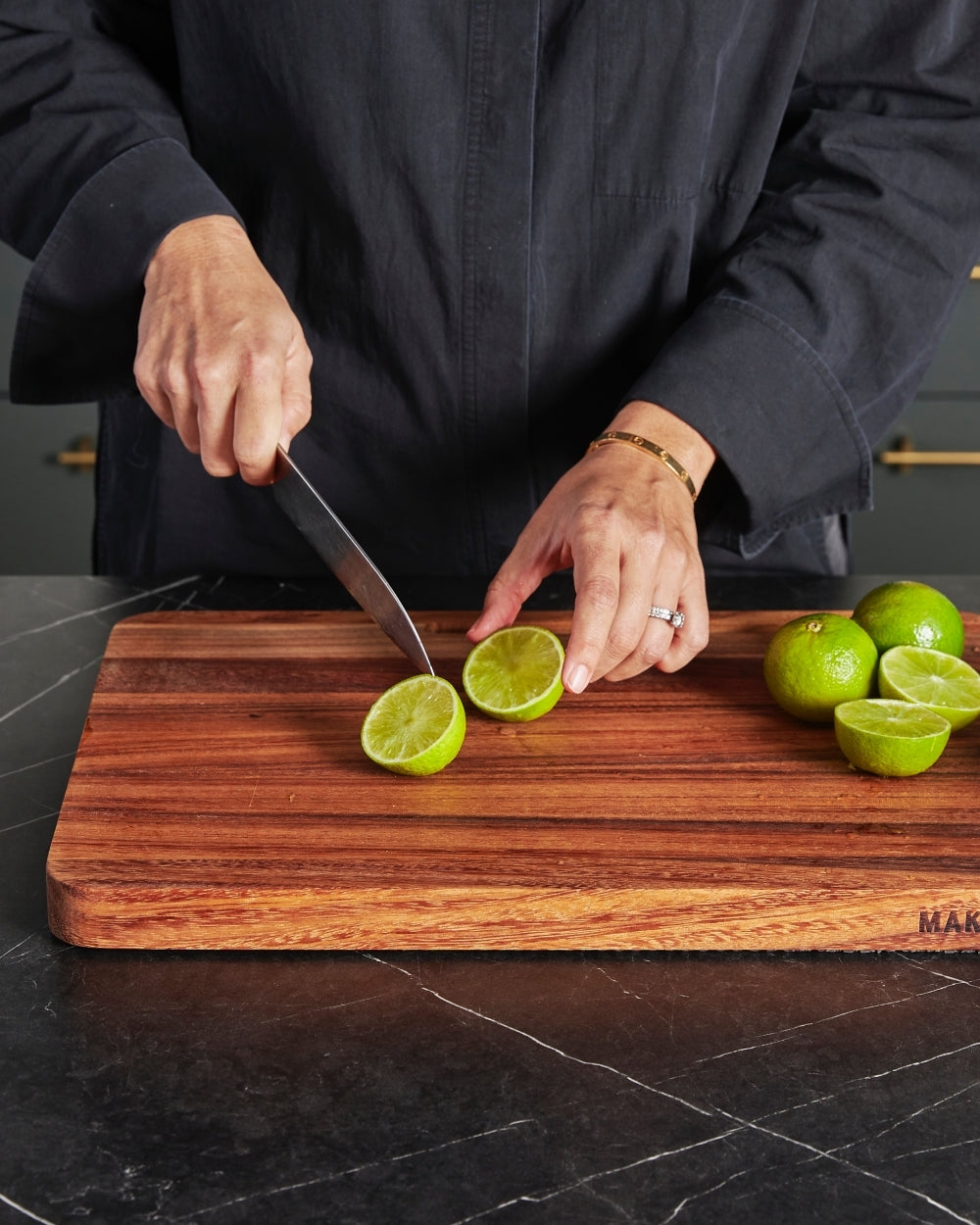 Person slicing limes on a wooden multi-use chopping board on a dark kitchen counter