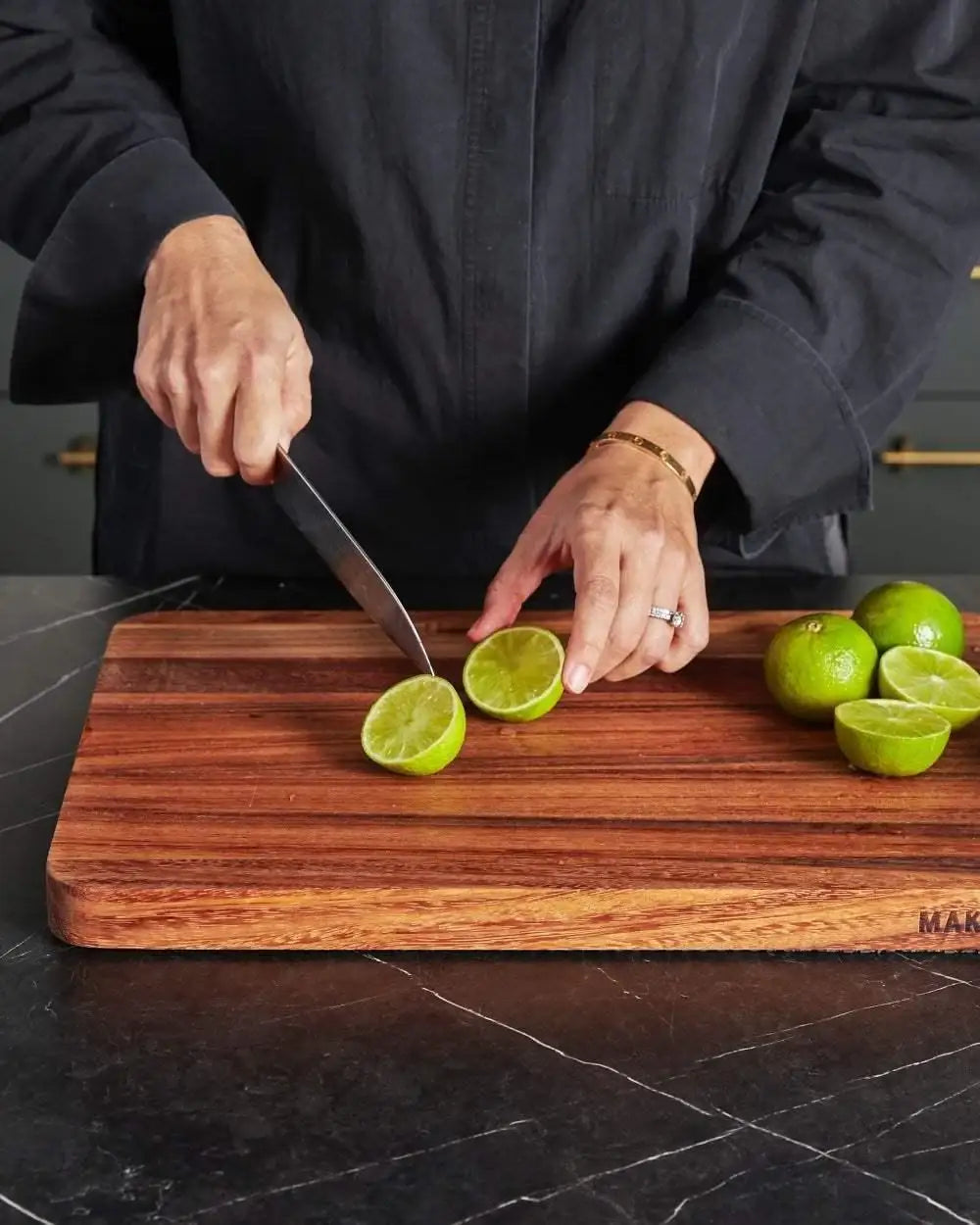 Hands slicing lime on a wooden Mako chopping board by chef Marion Grasby on black countertop