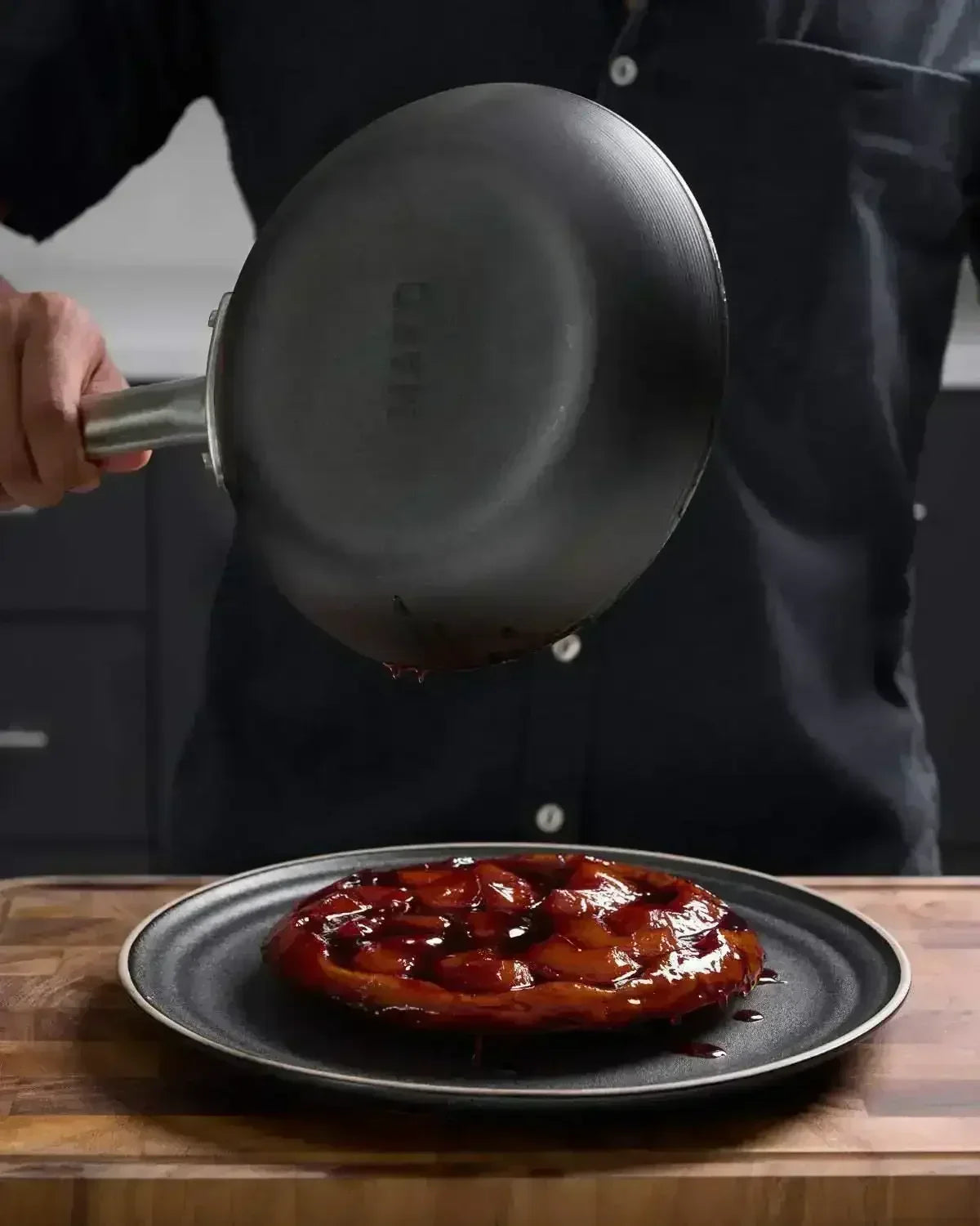 Black steel frying pan turning out caramelized tart onto plate on wooden board