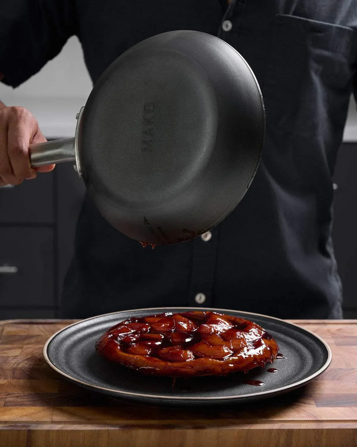 Person flipping a caramelized fruit tart onto a black plate using a Mako frying pan in a kitchen