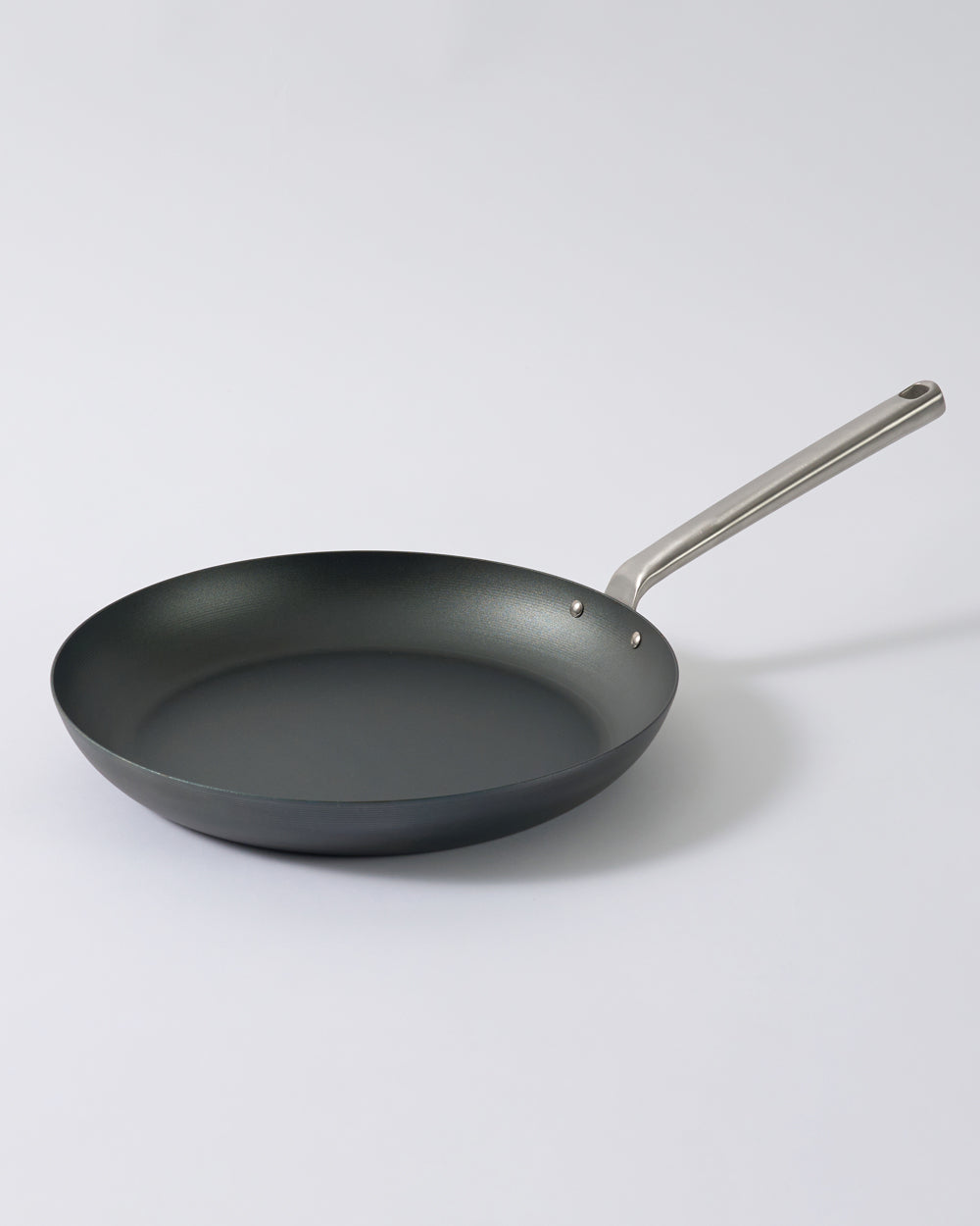 Black steel frying pan with stainless steel handle on a light background